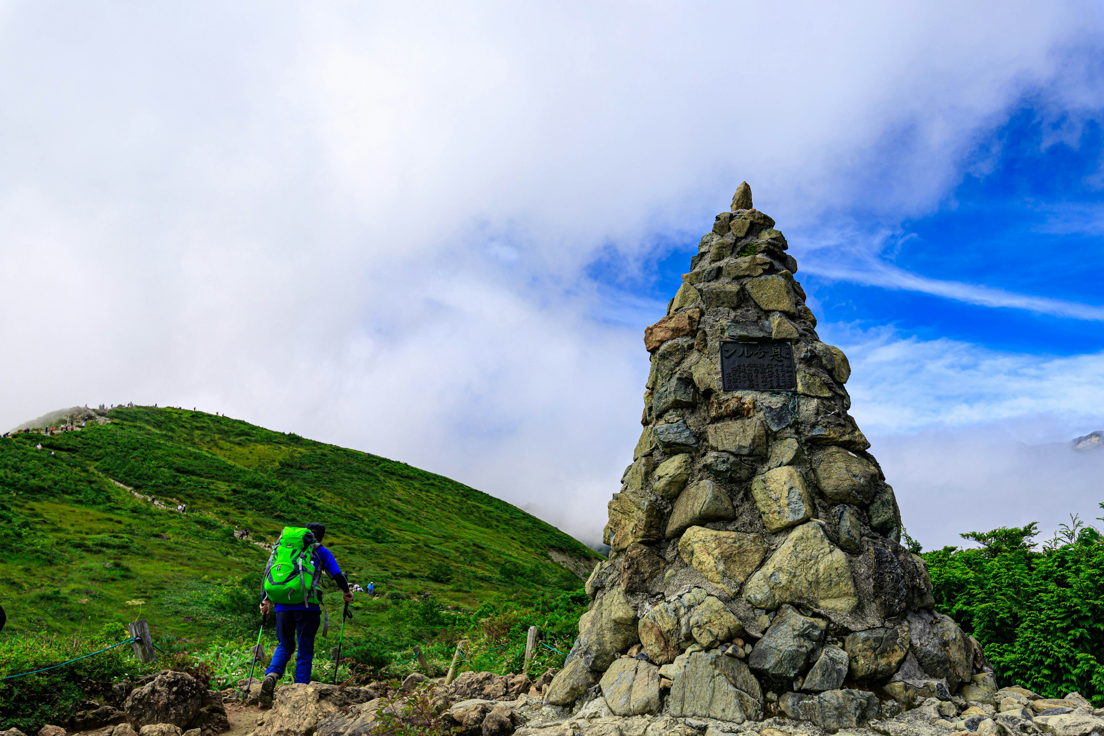 Hiker walking near a stone monument in a lush green landscape