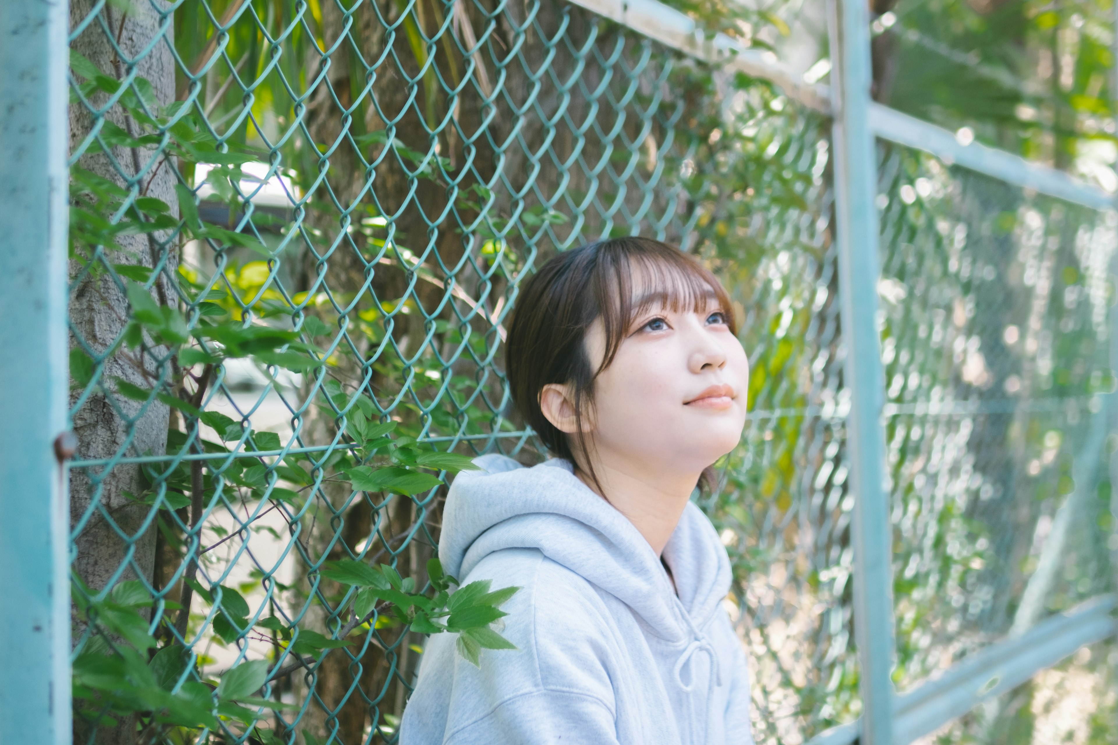 Jeune femme pensive devant une clôture verte entourée de feuilles