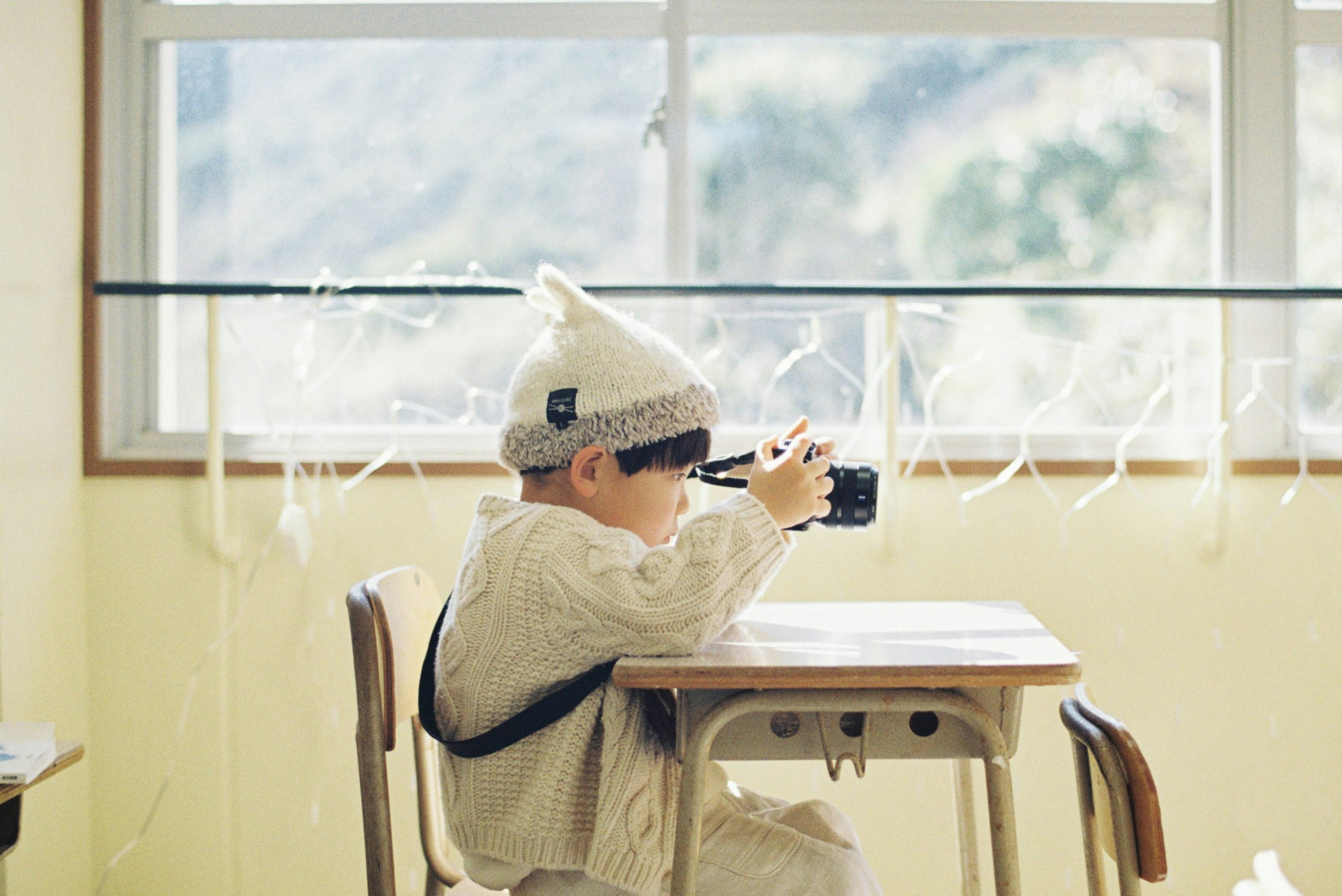 Bambino seduto a un tavolo che tiene una macchina fotografica in una stanza luminosa