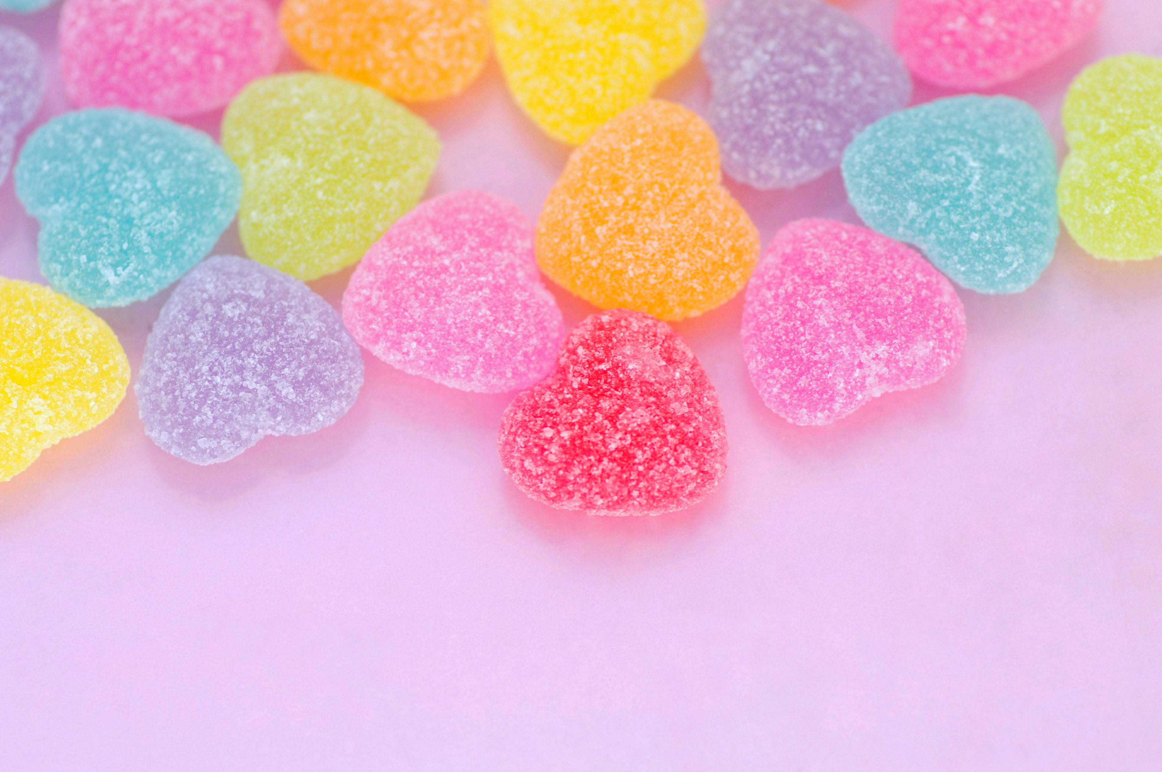 Dulces de gelatina en forma de corazón de colores esparcidos sobre un fondo rosa