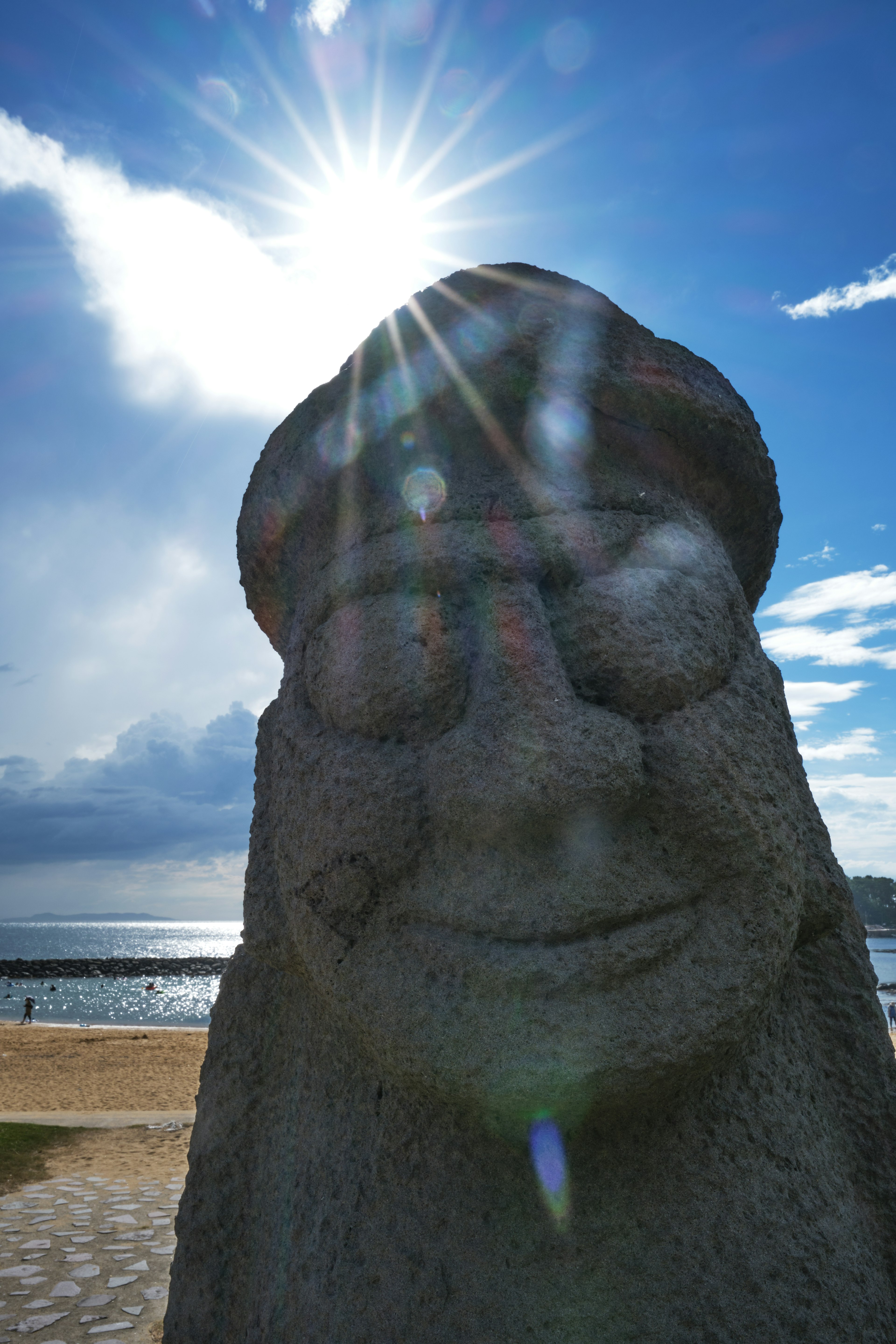 海のそばに立つ石の彫刻の顔と太陽の光