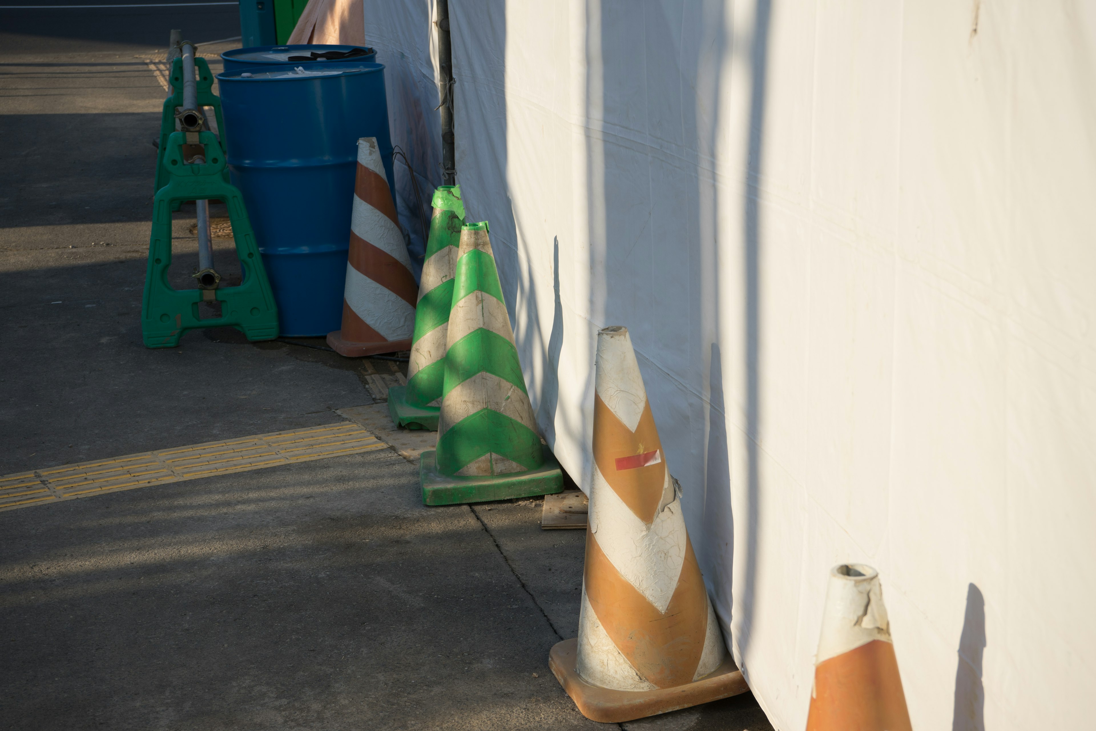 Colorful traffic cones and a blue barrel next to a white wall