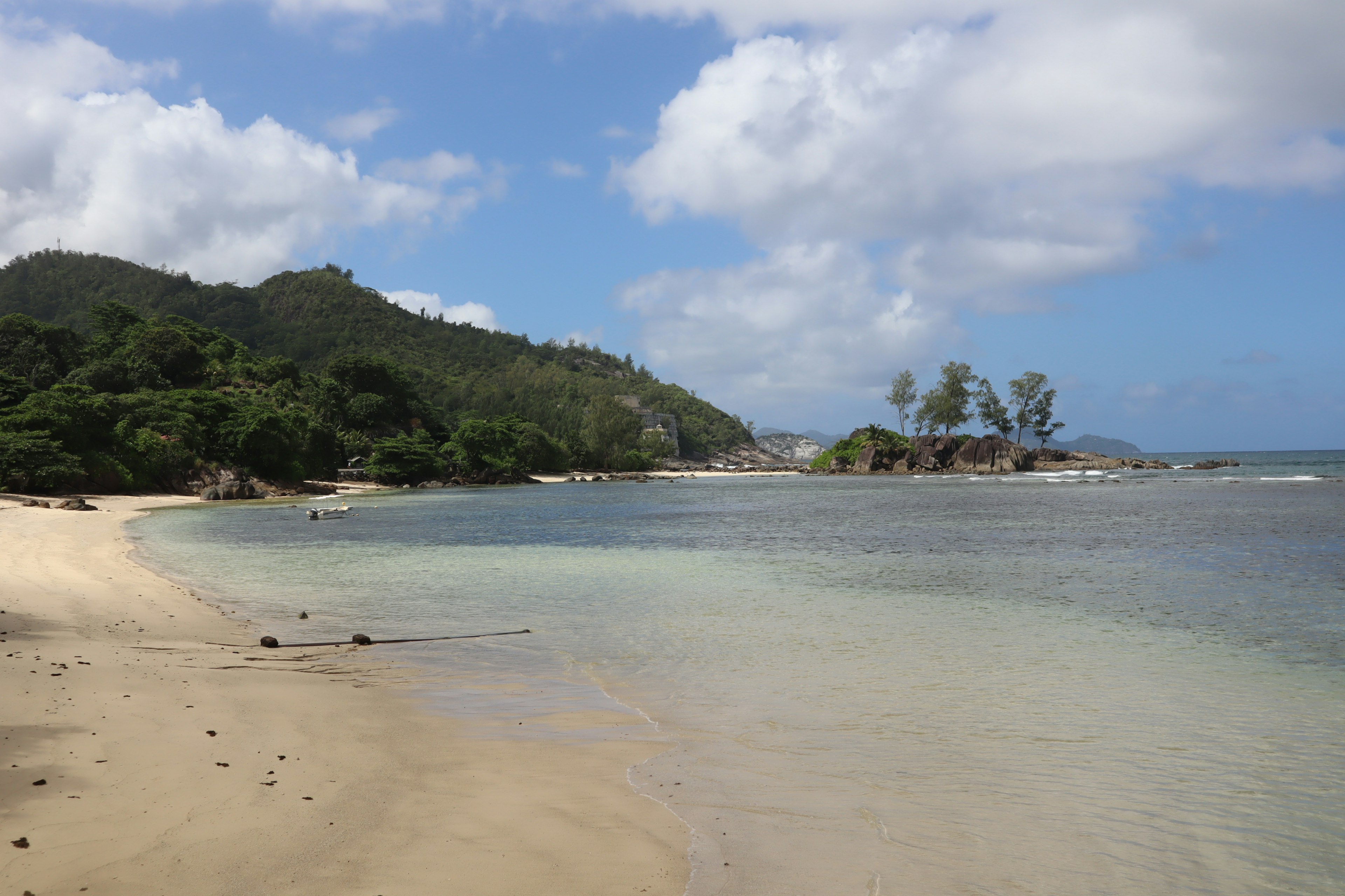 Scenic view of blue sea and sandy beach with green hills and blue sky