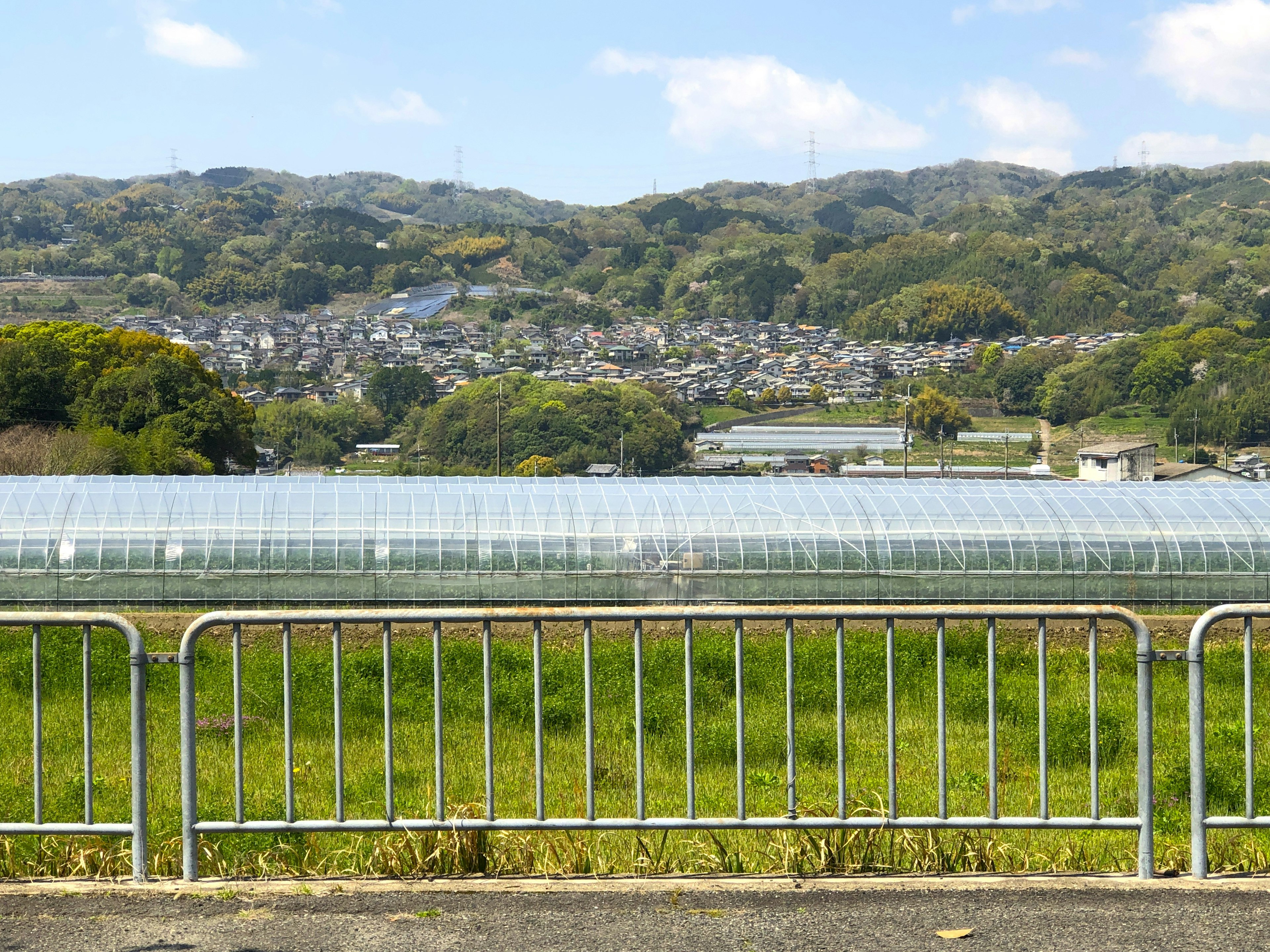 Expansive green field with transparent greenhouses in the foreground hills and a small town in the background