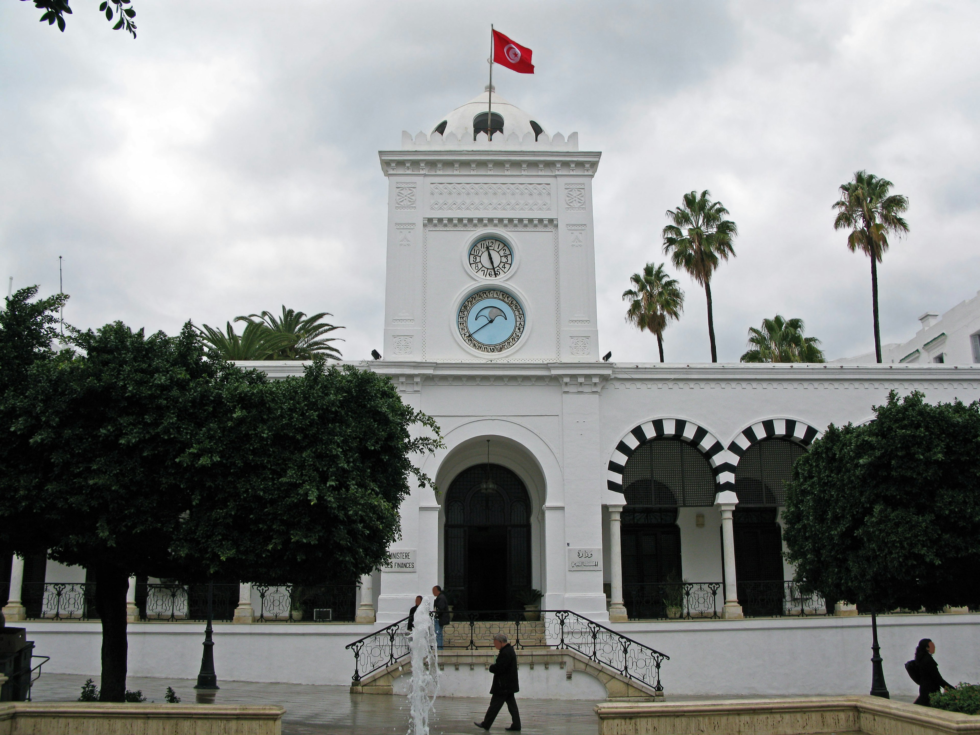 White building with a clock and palm trees in front