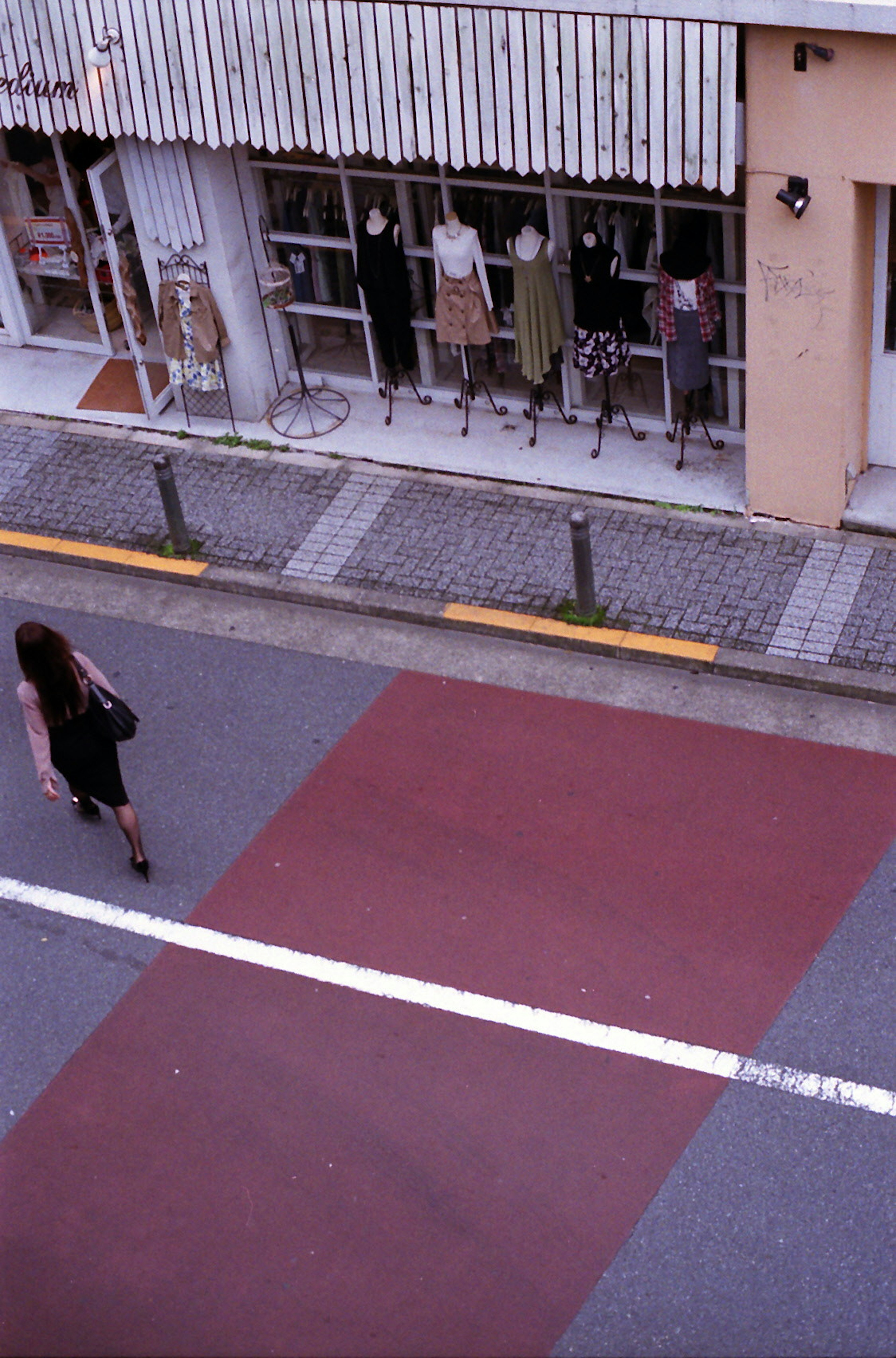 A woman walking on a red-striped sidewalk with storefront displays