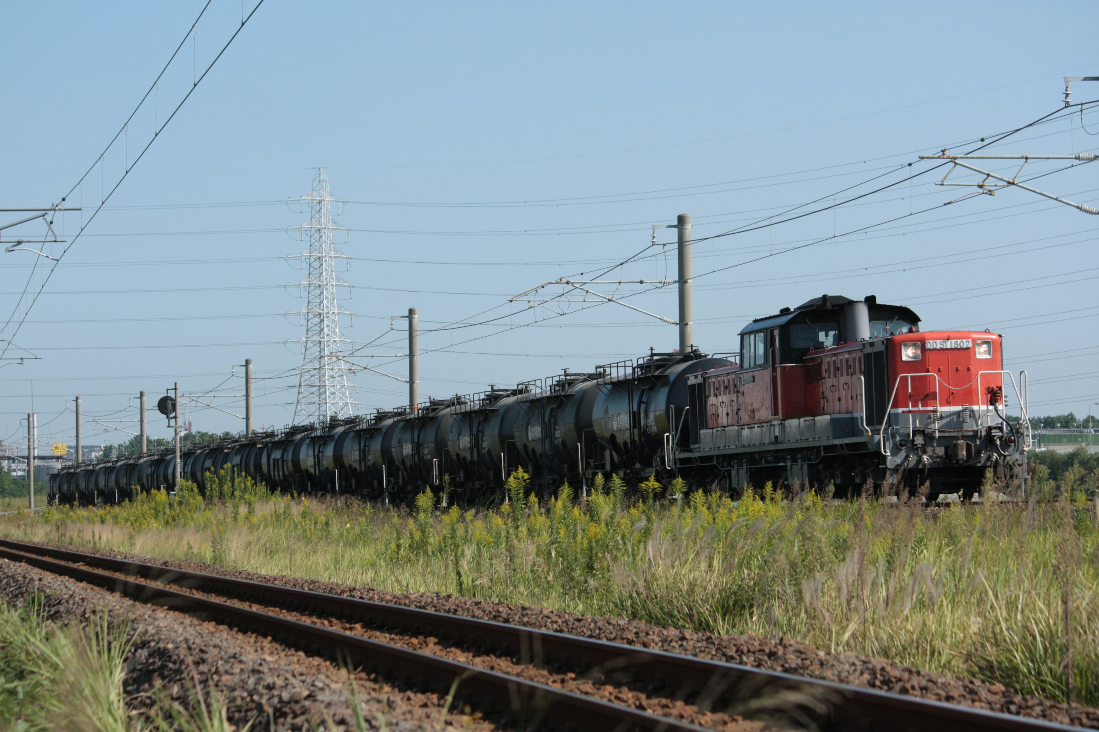 Rote Lokomotive zieht einen Güterzug auf Gleisen mit Gras in der Nähe