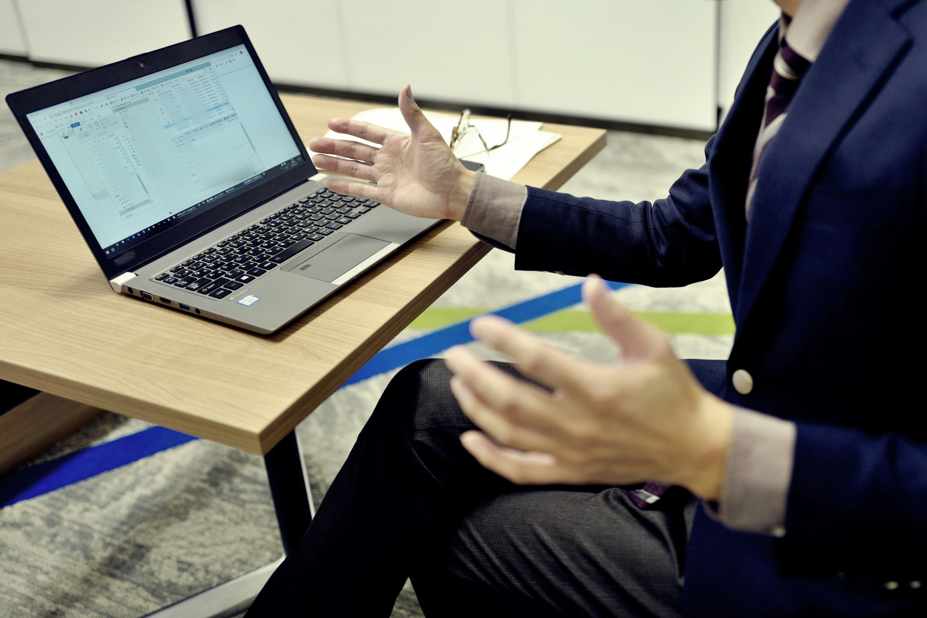 A man in a business suit gesturing in front of a laptop