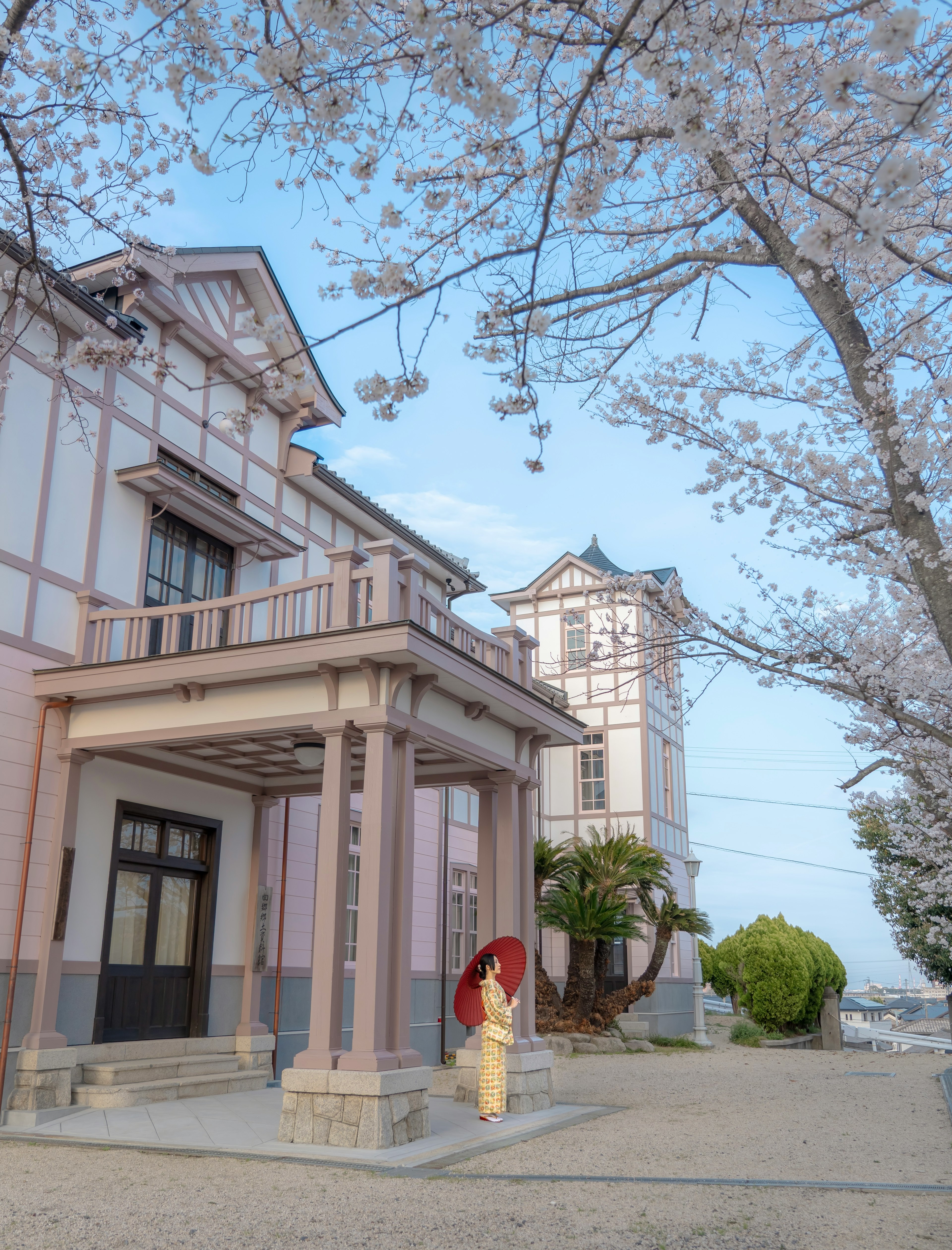 Edificio histórico con cerezos en flor y una mujer con un paraguas tradicional