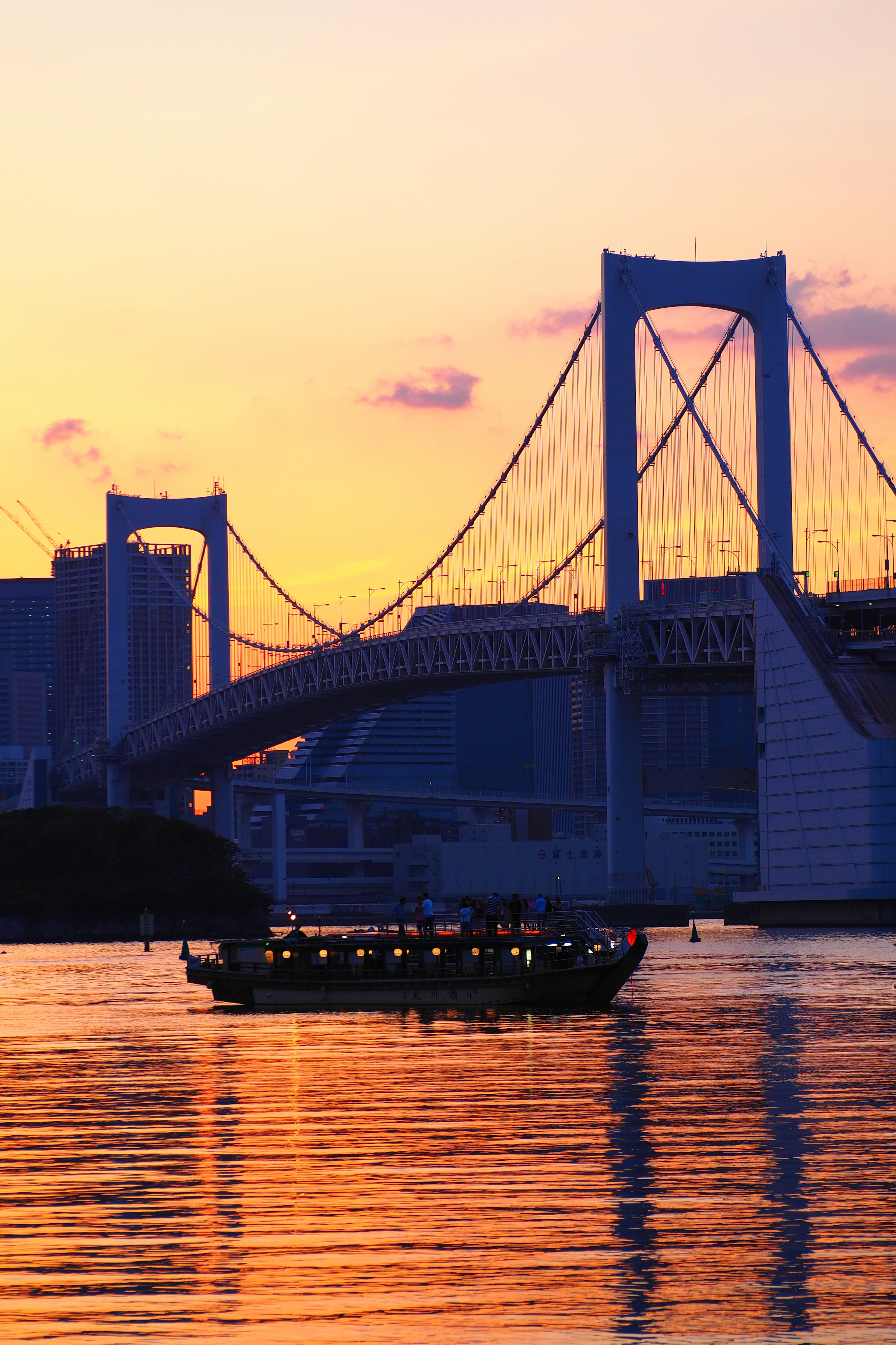 Sonnenuntergangsansicht der Rainbow Bridge mit einem Boot auf ruhigem Wasser