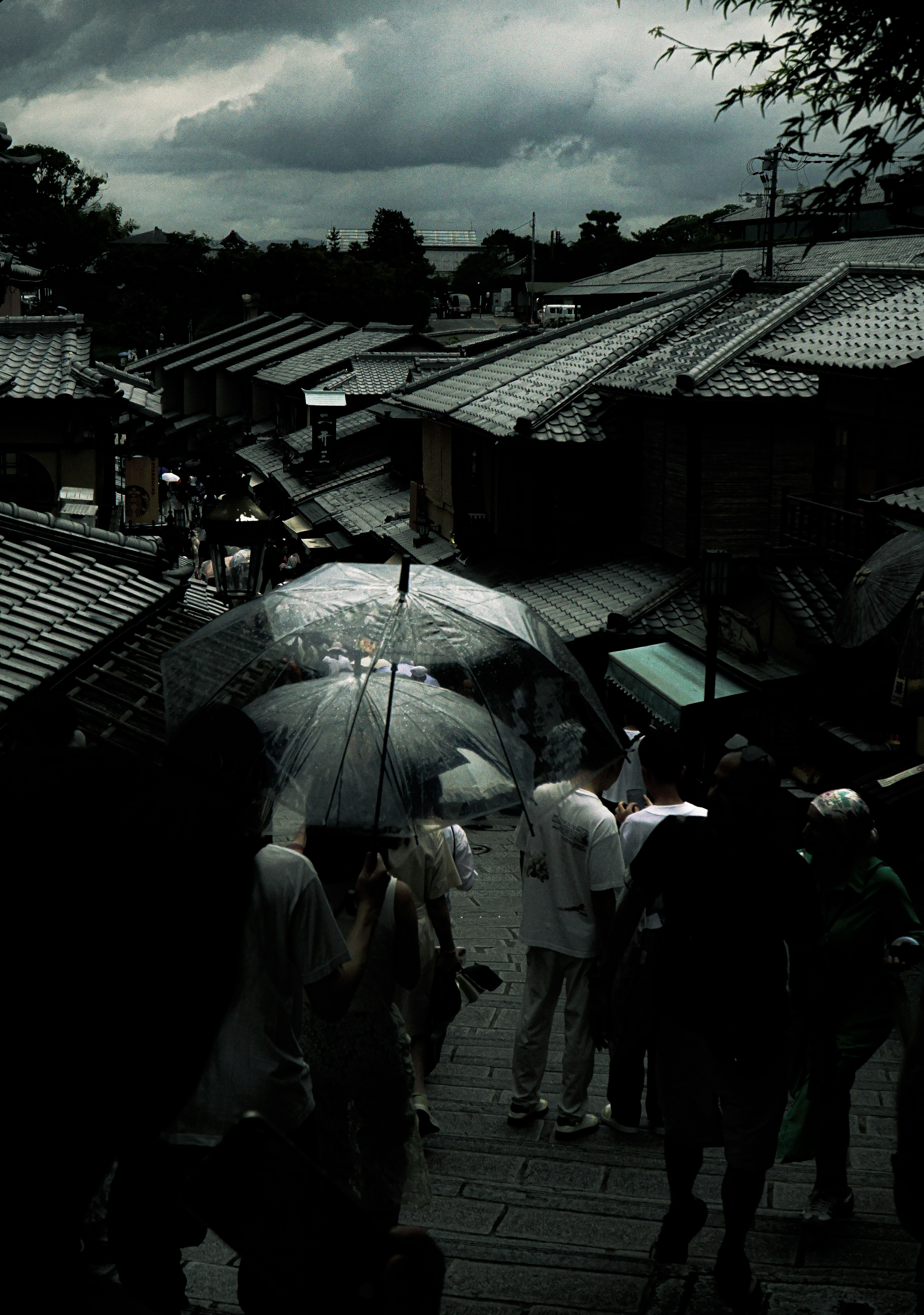 暗い雲の下で傘を持った人々が歩く古い街並み