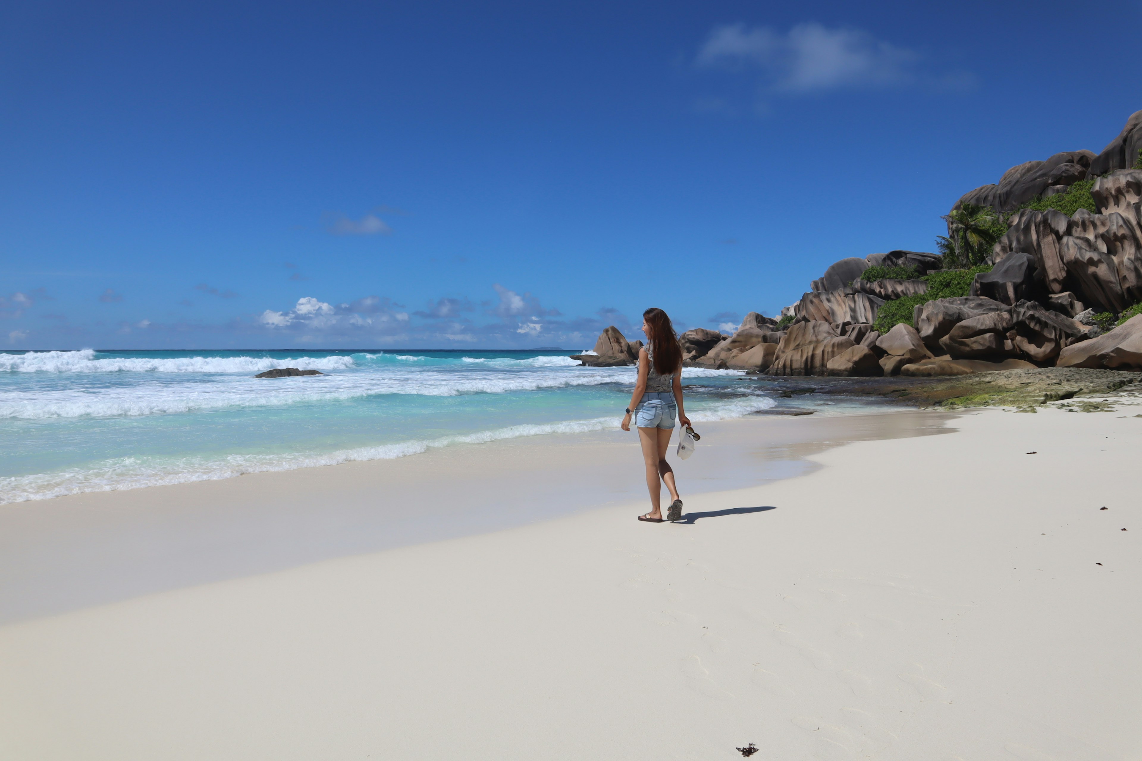 Eine Frau, die an einem Strand mit blauem Ozean und weißem Sand geht