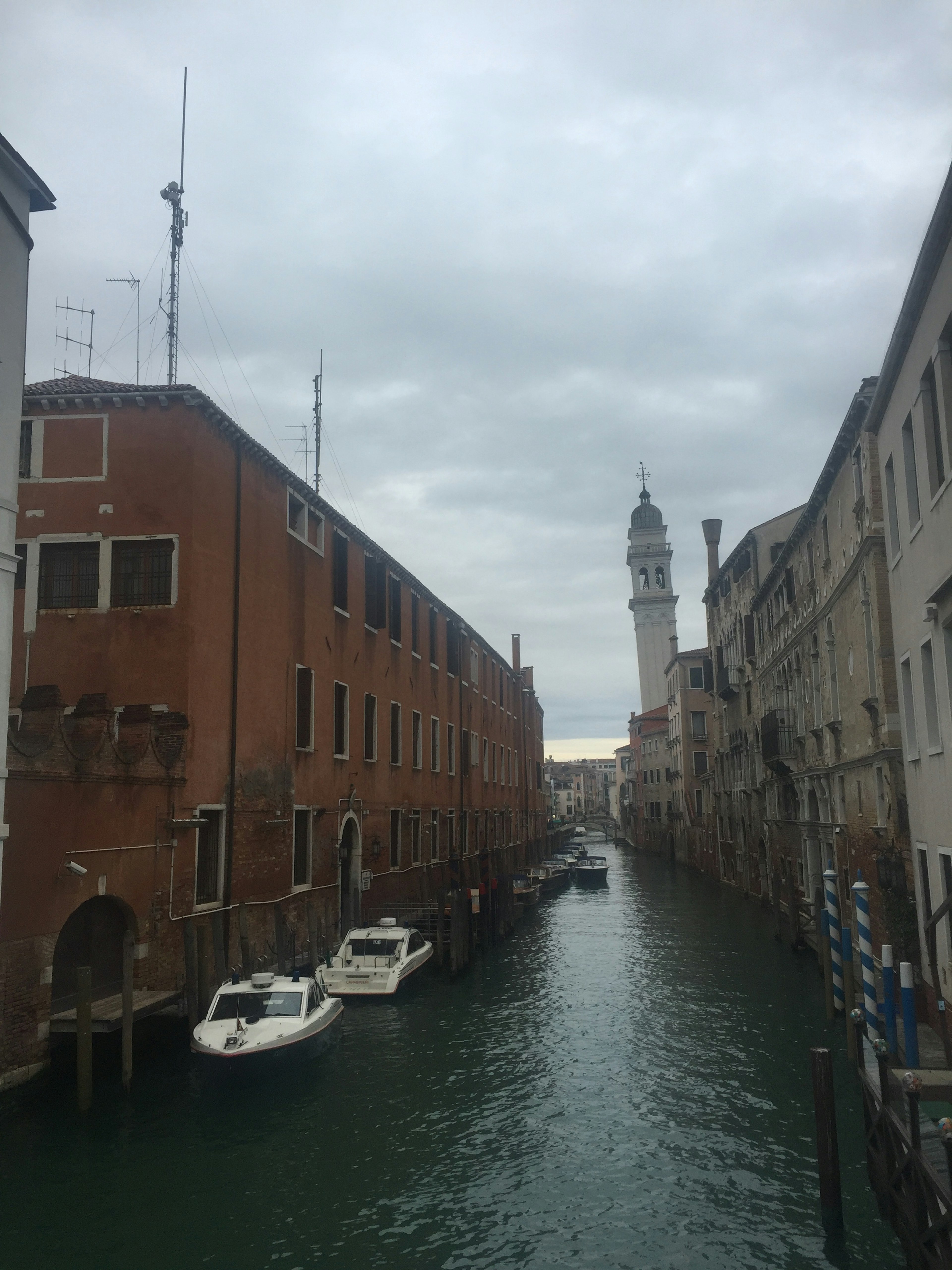 Kanal Venesia dengan bangunan bata merah dan perahu di bawah langit abu-abu dengan menara