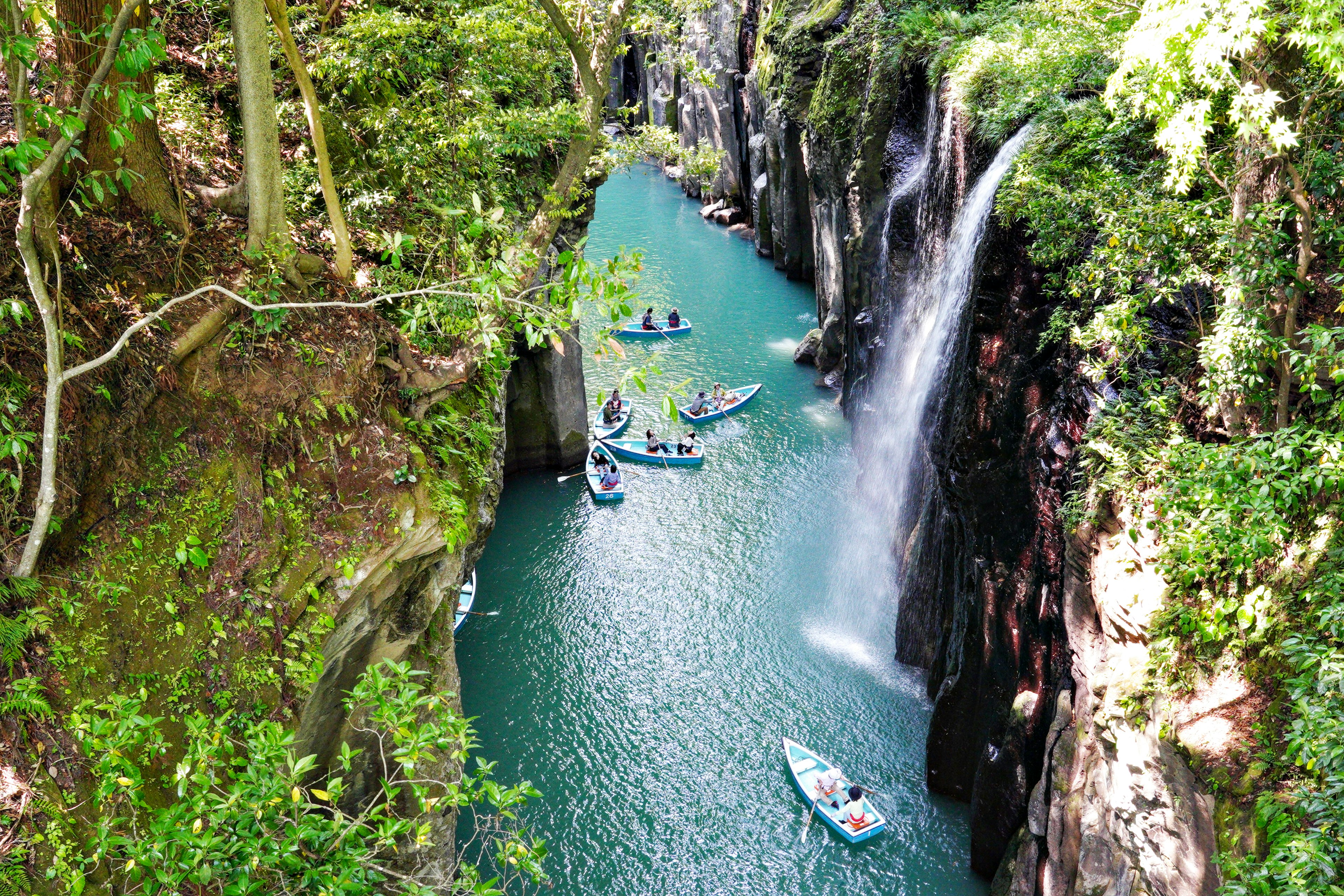 Scenic view of a lush canyon with a blue river and waterfall small boats floating