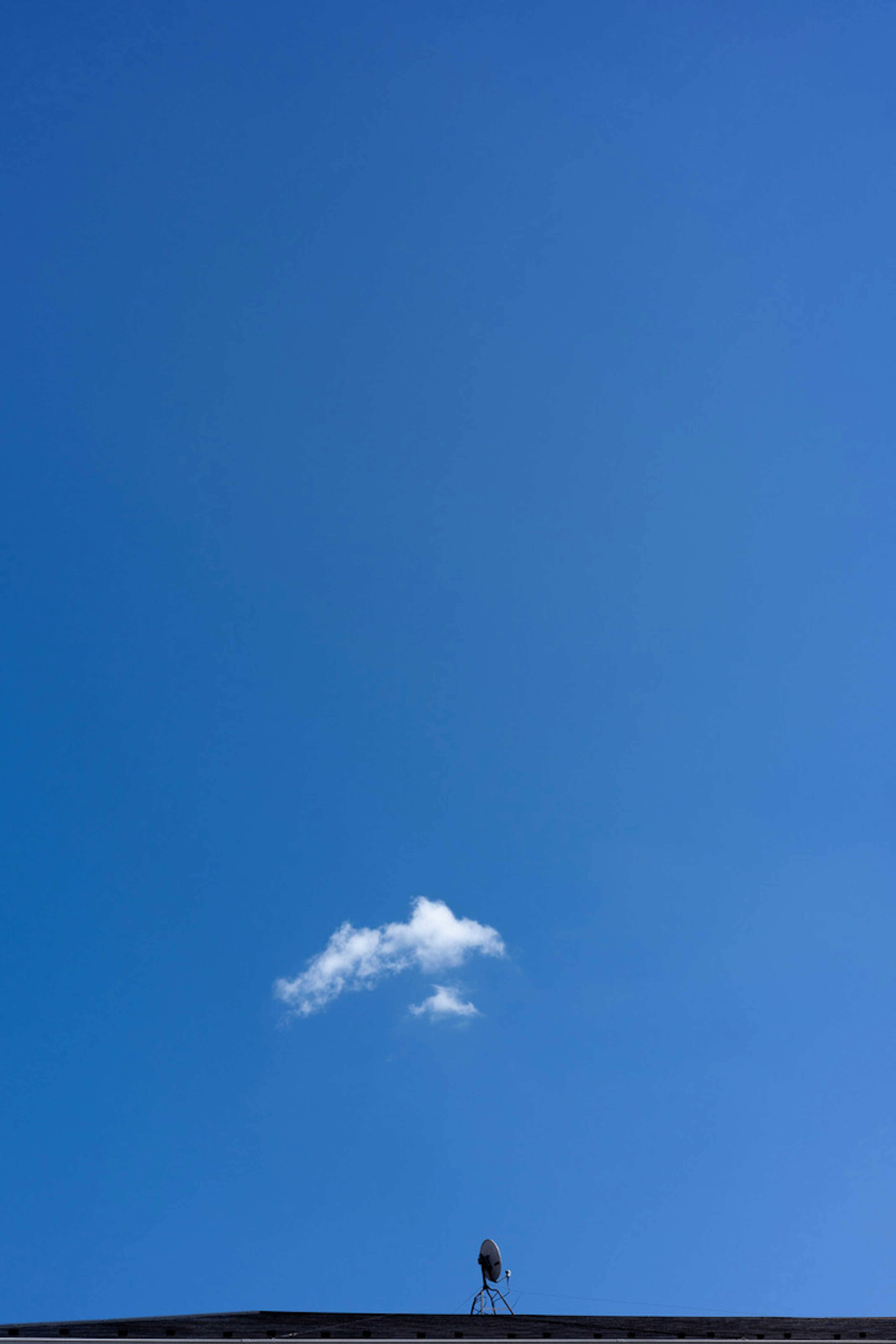 Eine kleine weiße Wolke in einem blauen Himmel mit einem Vogel auf einem Dach