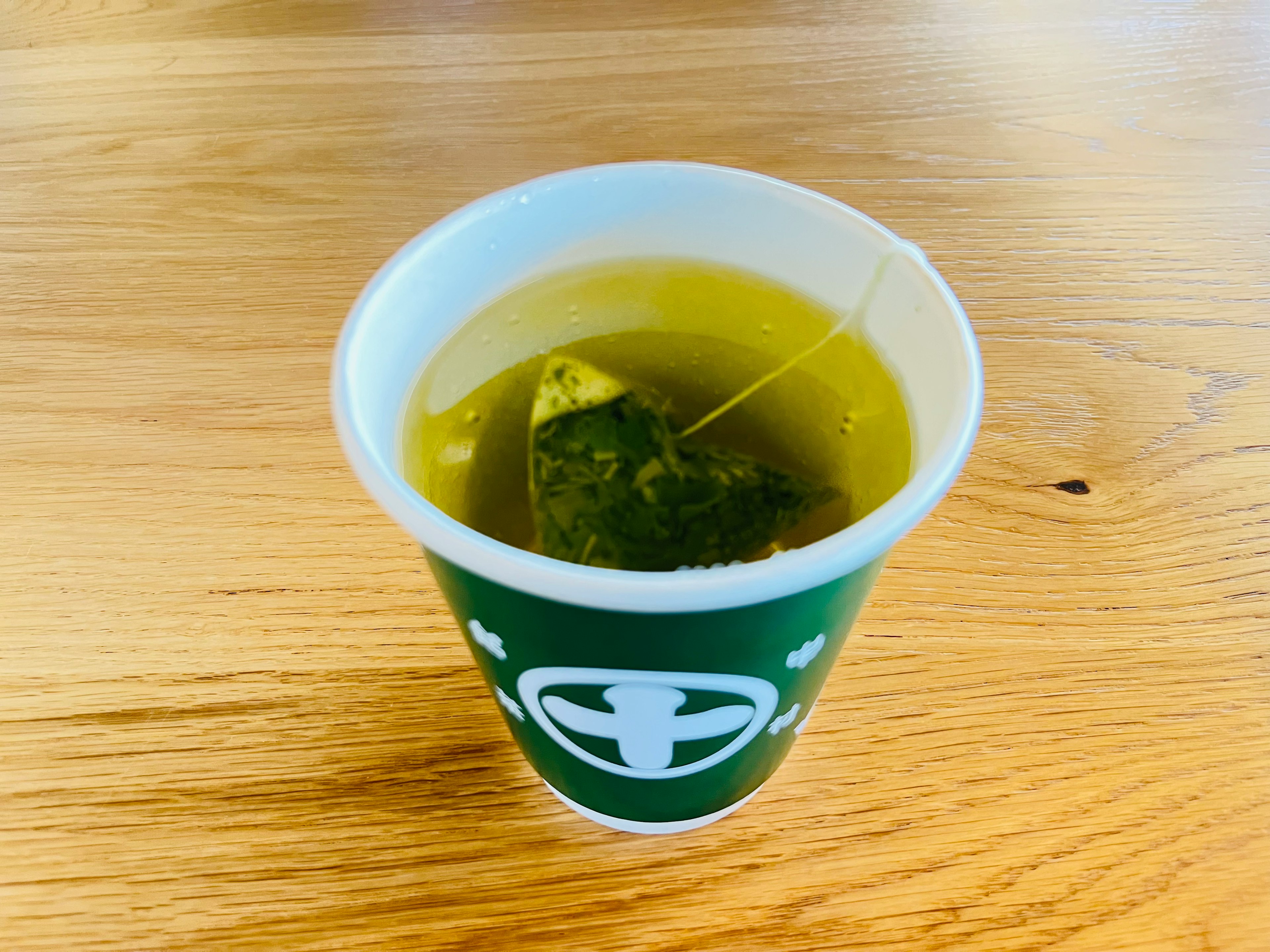 Une tasse de thé vert avec un sachet de thé sur une table en bois