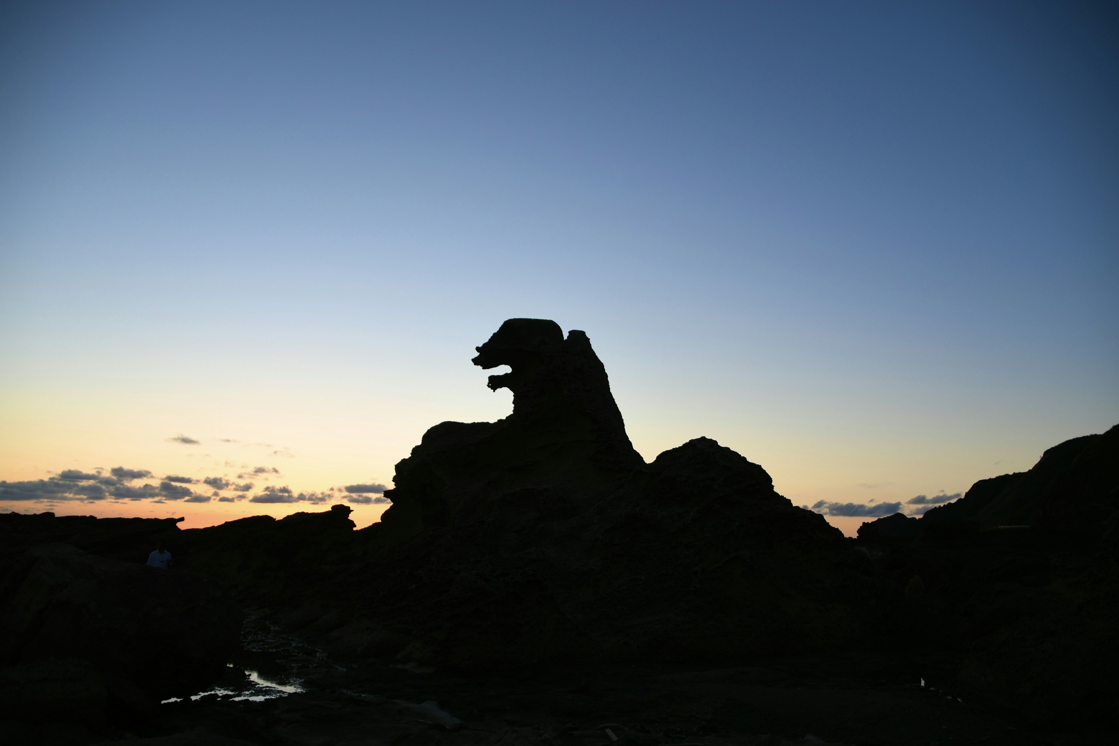 夕焼けの中でシルエットが際立つ岩の形がライオンのように見える