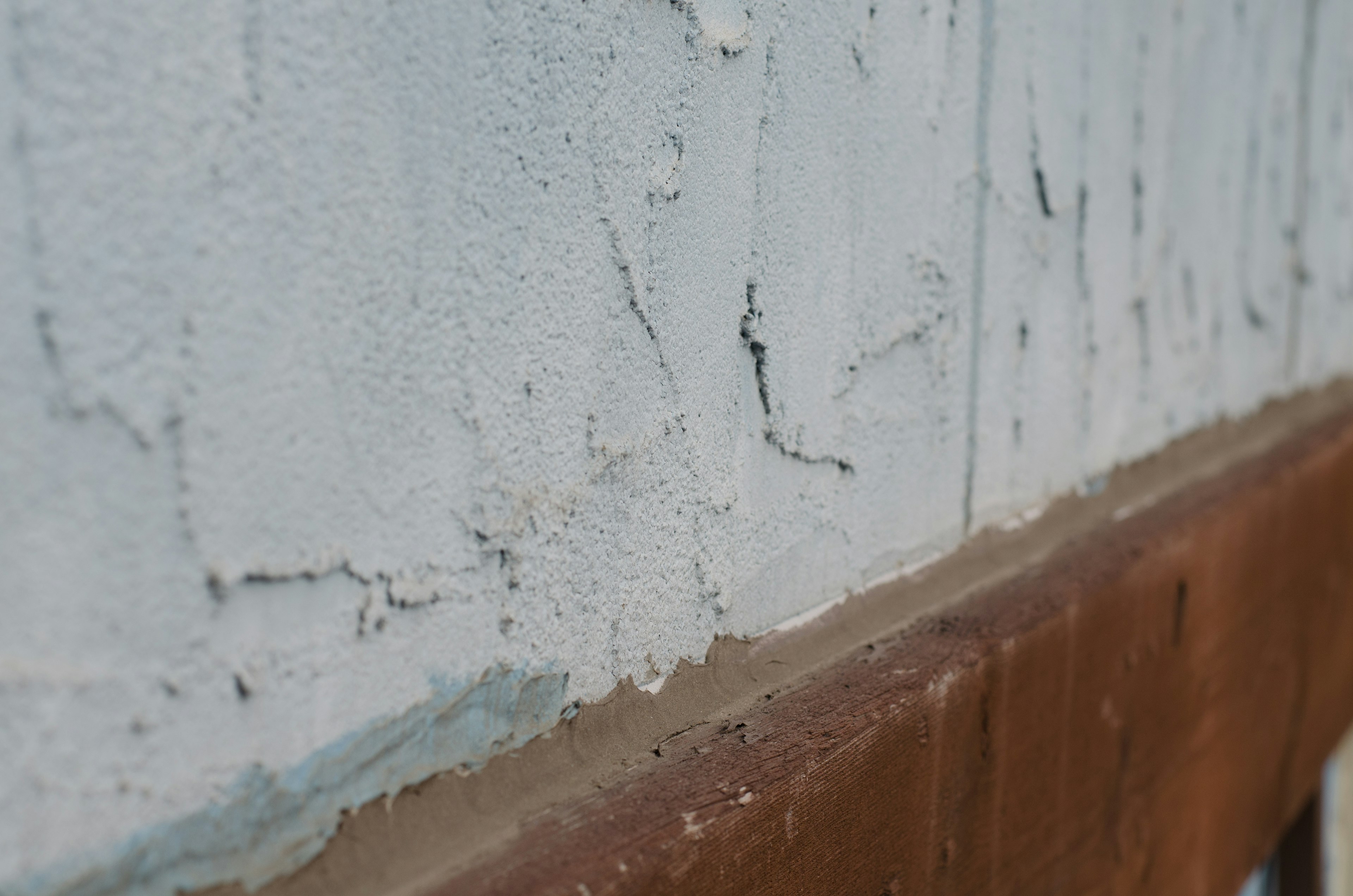 Primer plano de una pared blanca con grietas y una base marrón