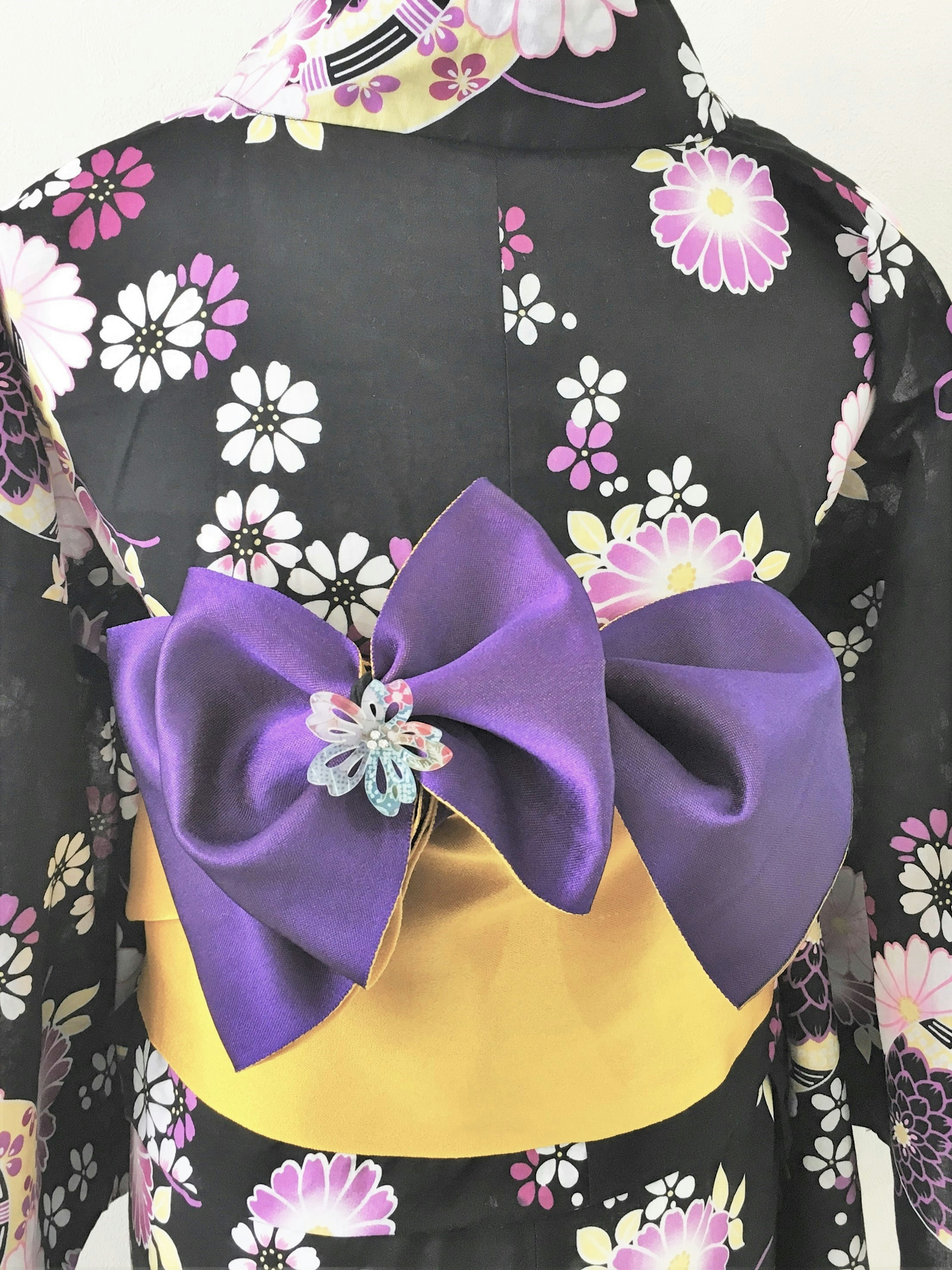 Un kimono floral negro con un obi amarillo y un gran lazo morado