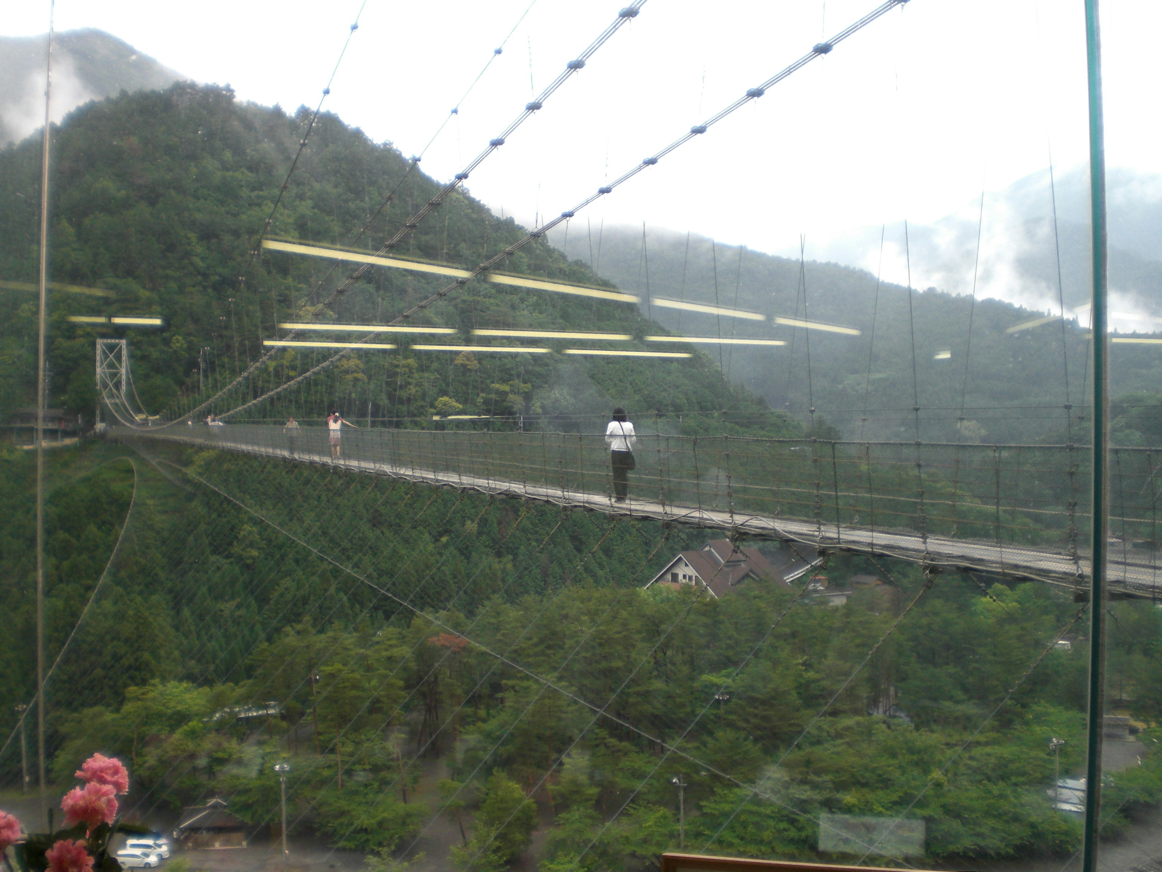 Eine Person, die über eine transparente Hängebrücke mit Bergen im Hintergrund geht