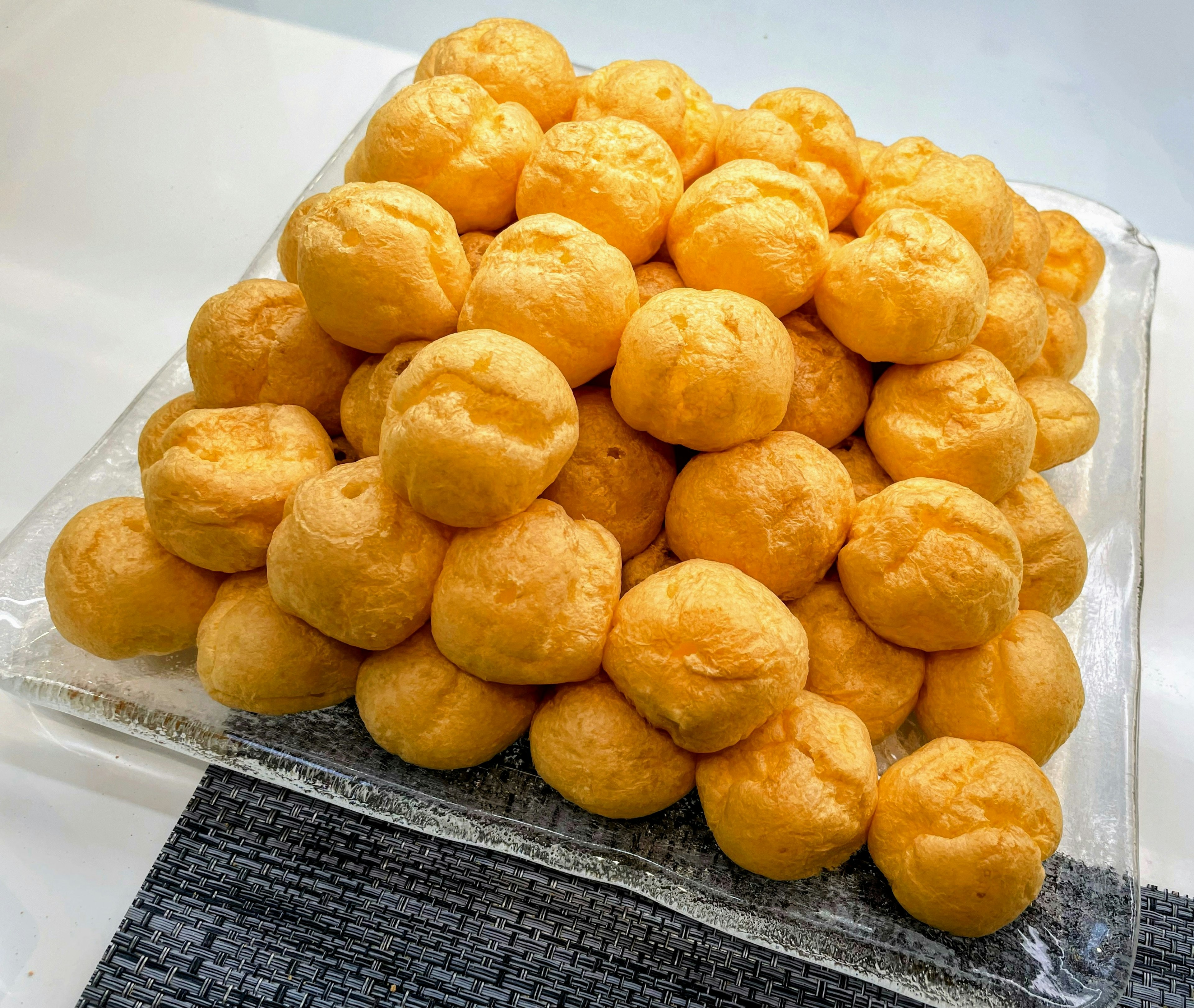 A large pile of yellow cream puffs on a glass plate