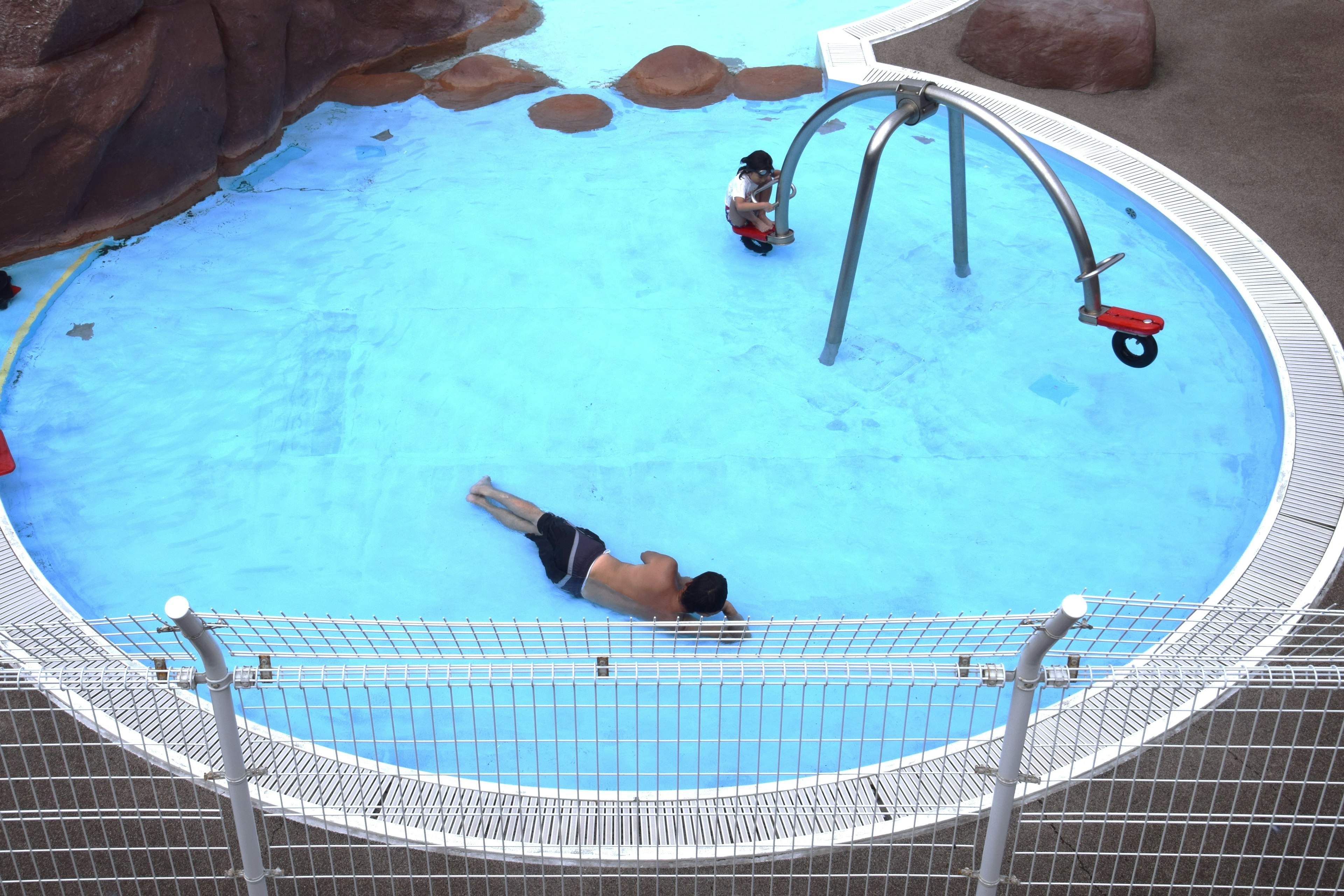 Eine Szene von Kindern und einem Erwachsenen, die in einem blauen Wasserpool spielen