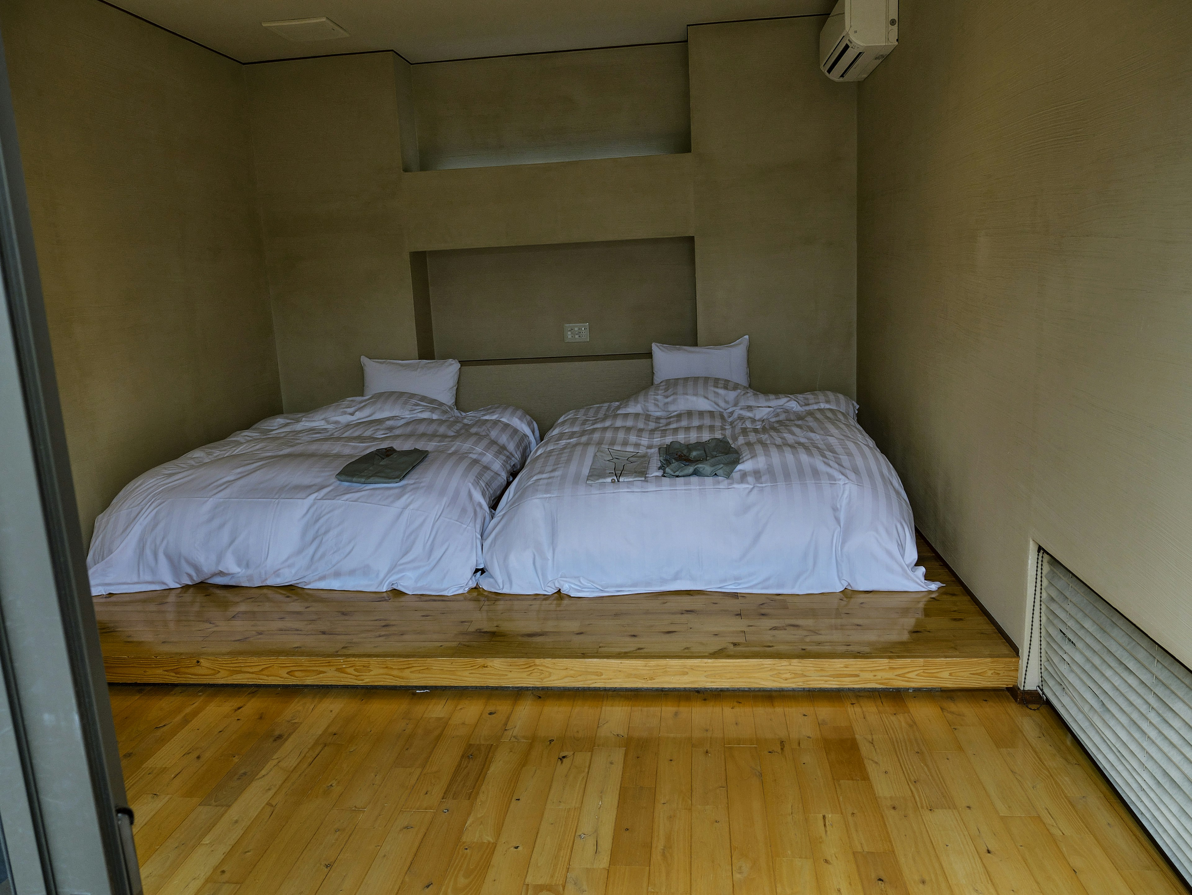 Simple bedroom featuring two beds with white bedding and wooden floor