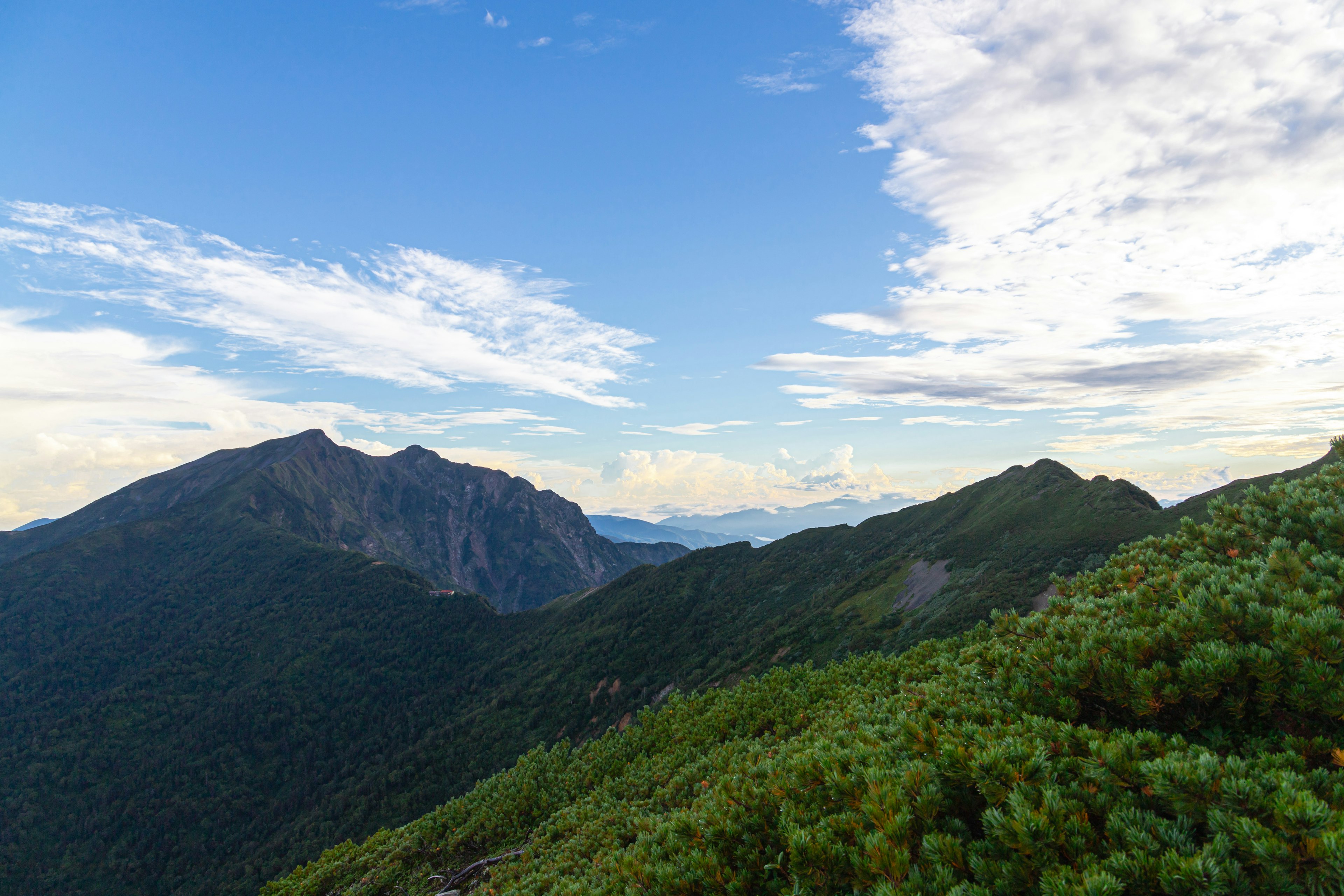 Vista escénica de montañas verdes bajo un cielo azul con nubes blancas