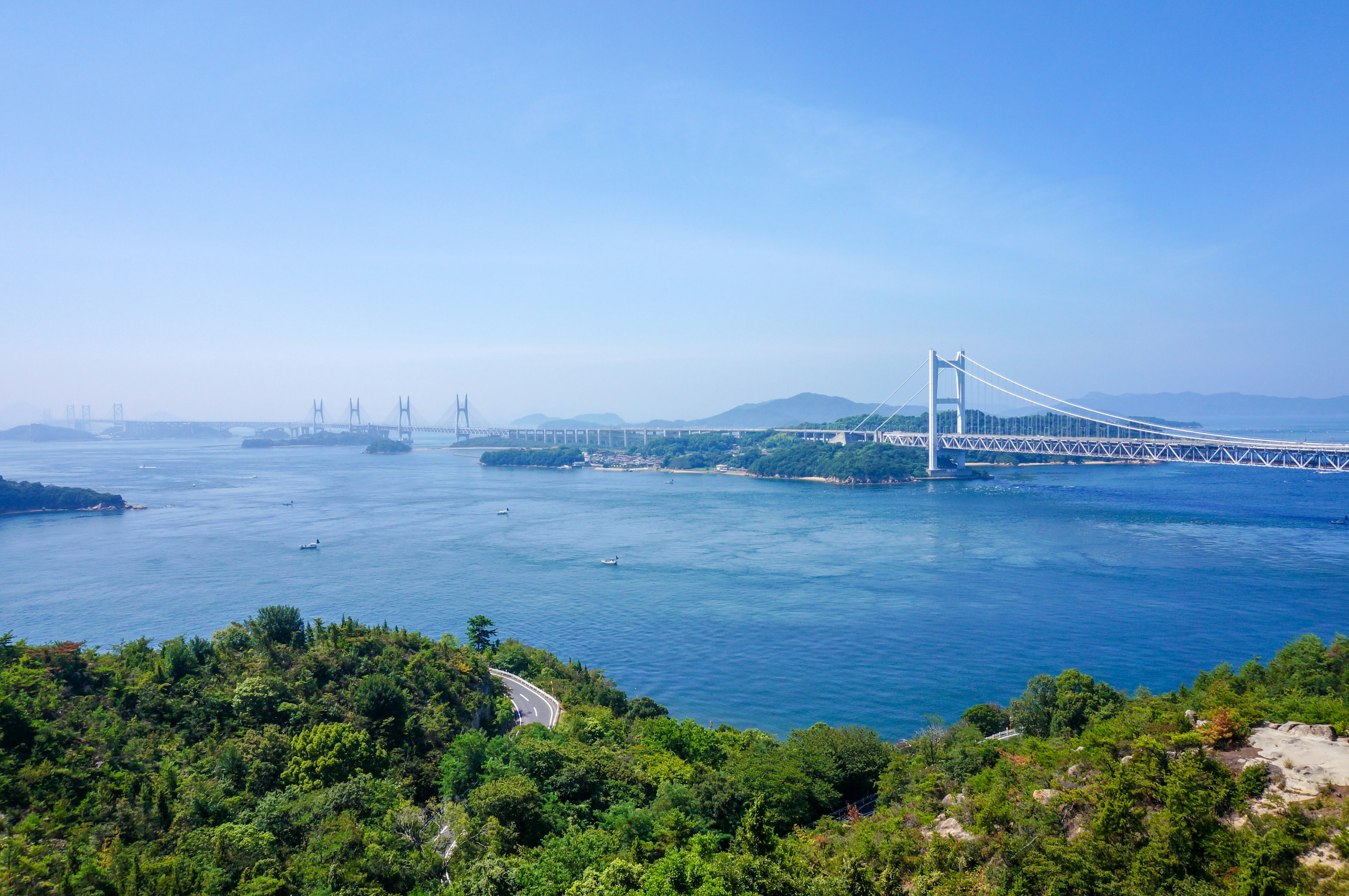 Panoramablick auf ein blaues Meer mit grünen Hügeln und einer Brücke