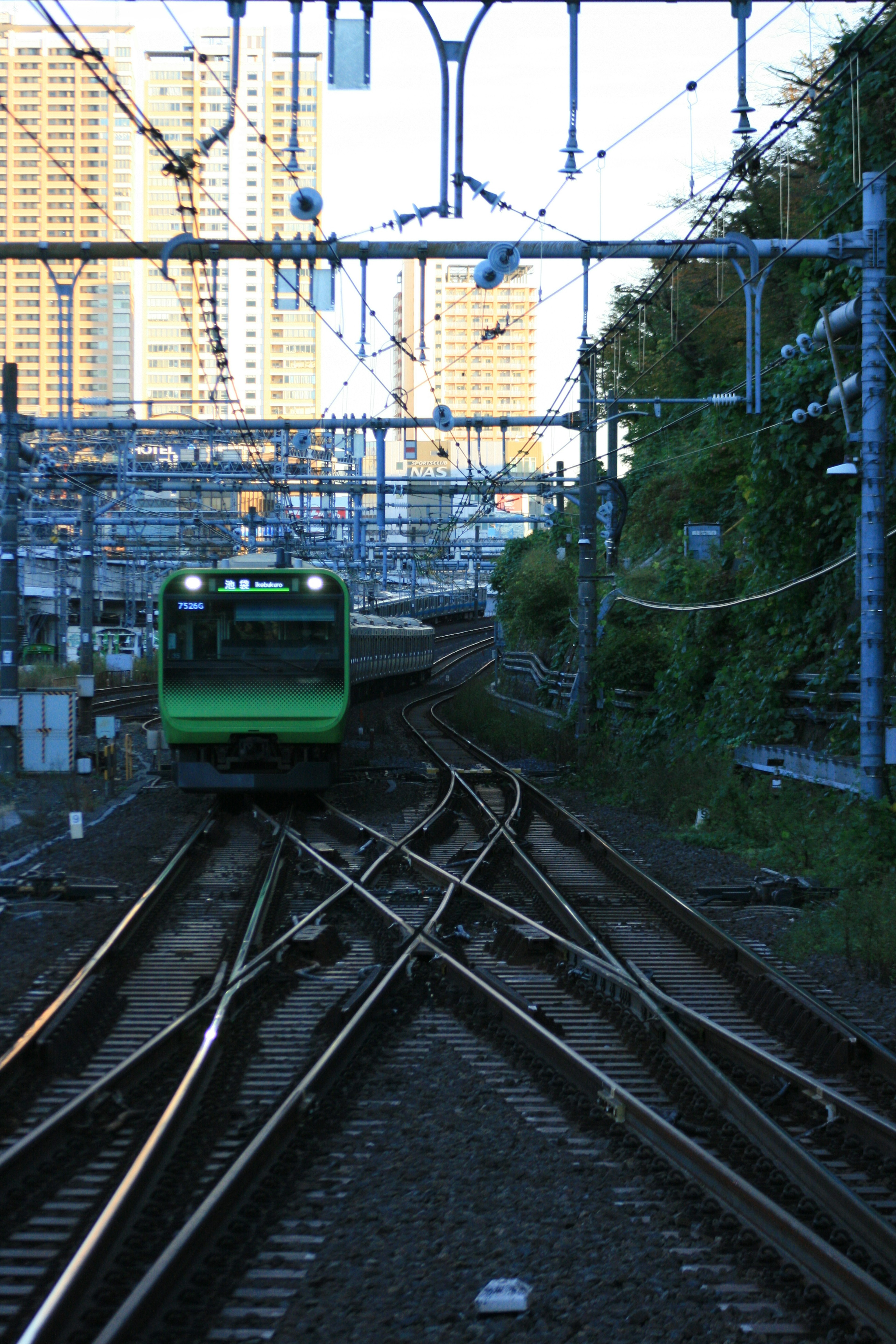 Green train navigating through intersecting tracks in an urban landscape