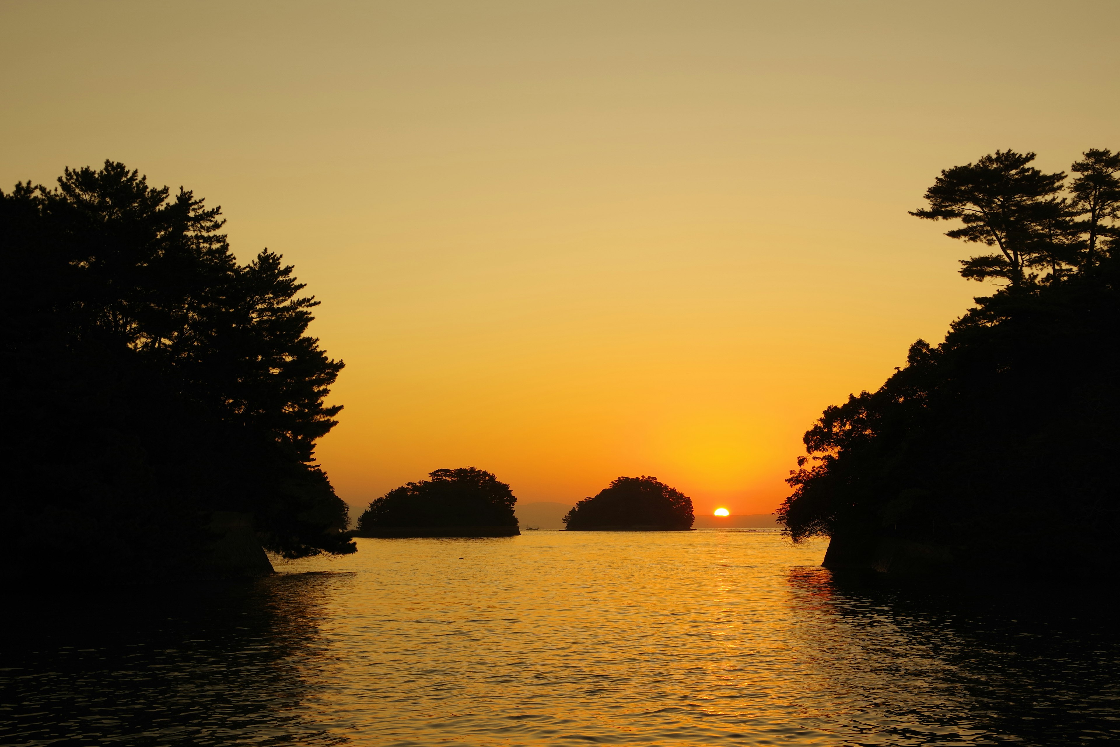 Scenic view of sunset over water with silhouettes of islands and trees