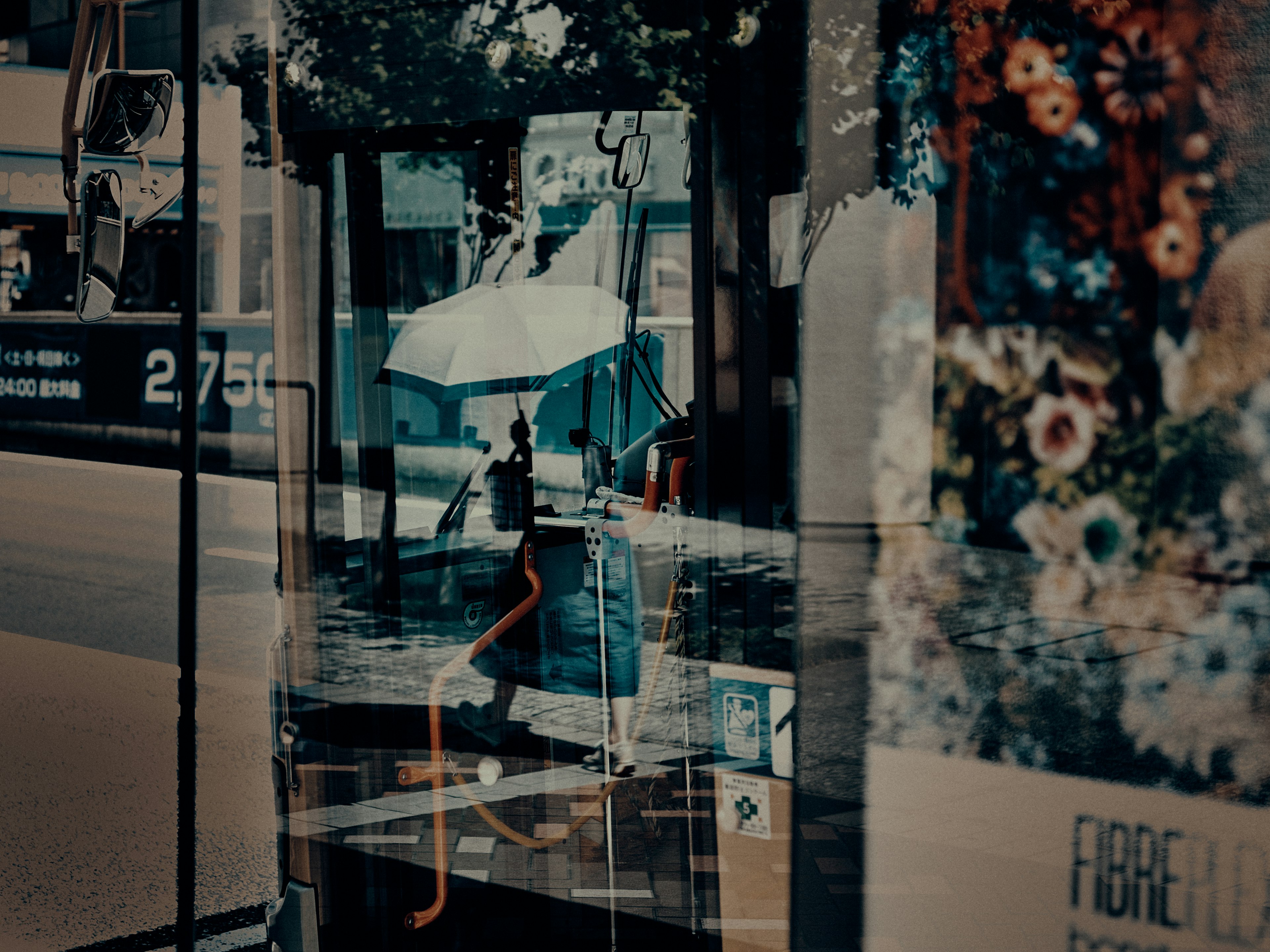 傘を持った人が雨の中を歩いている様子の反射が映る街の風景