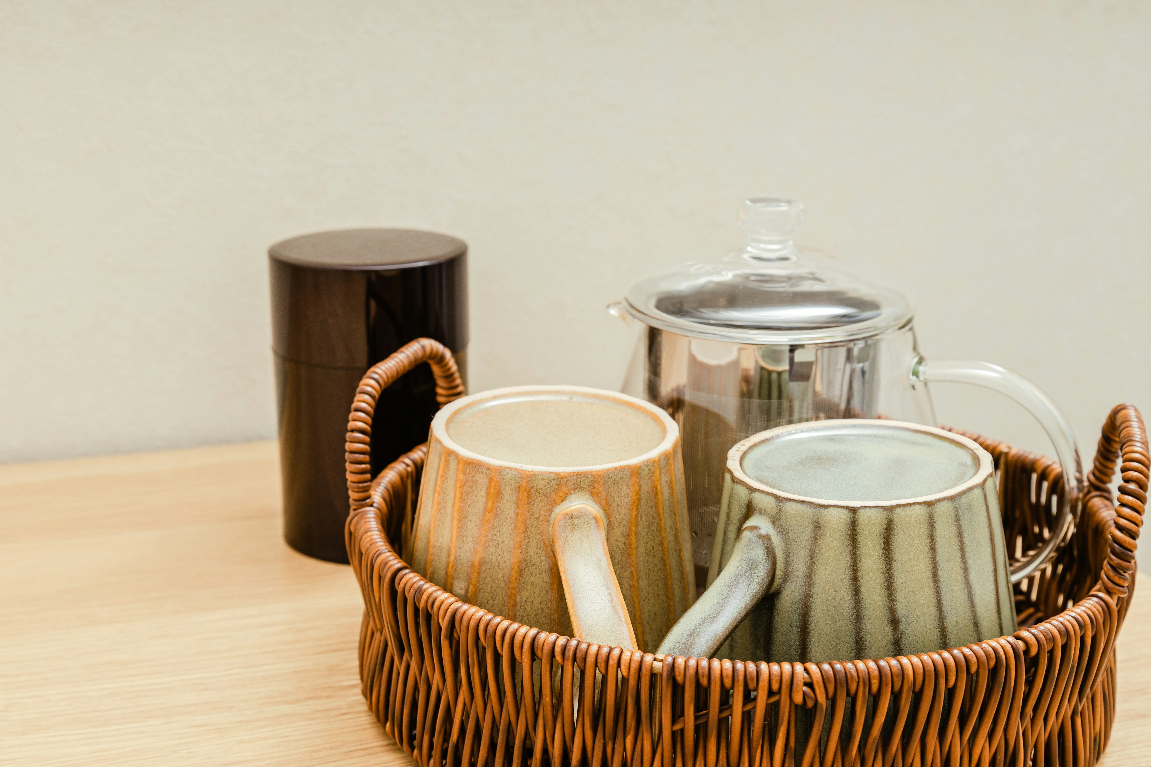 Ceramic mugs and a silver teapot arranged in a basket