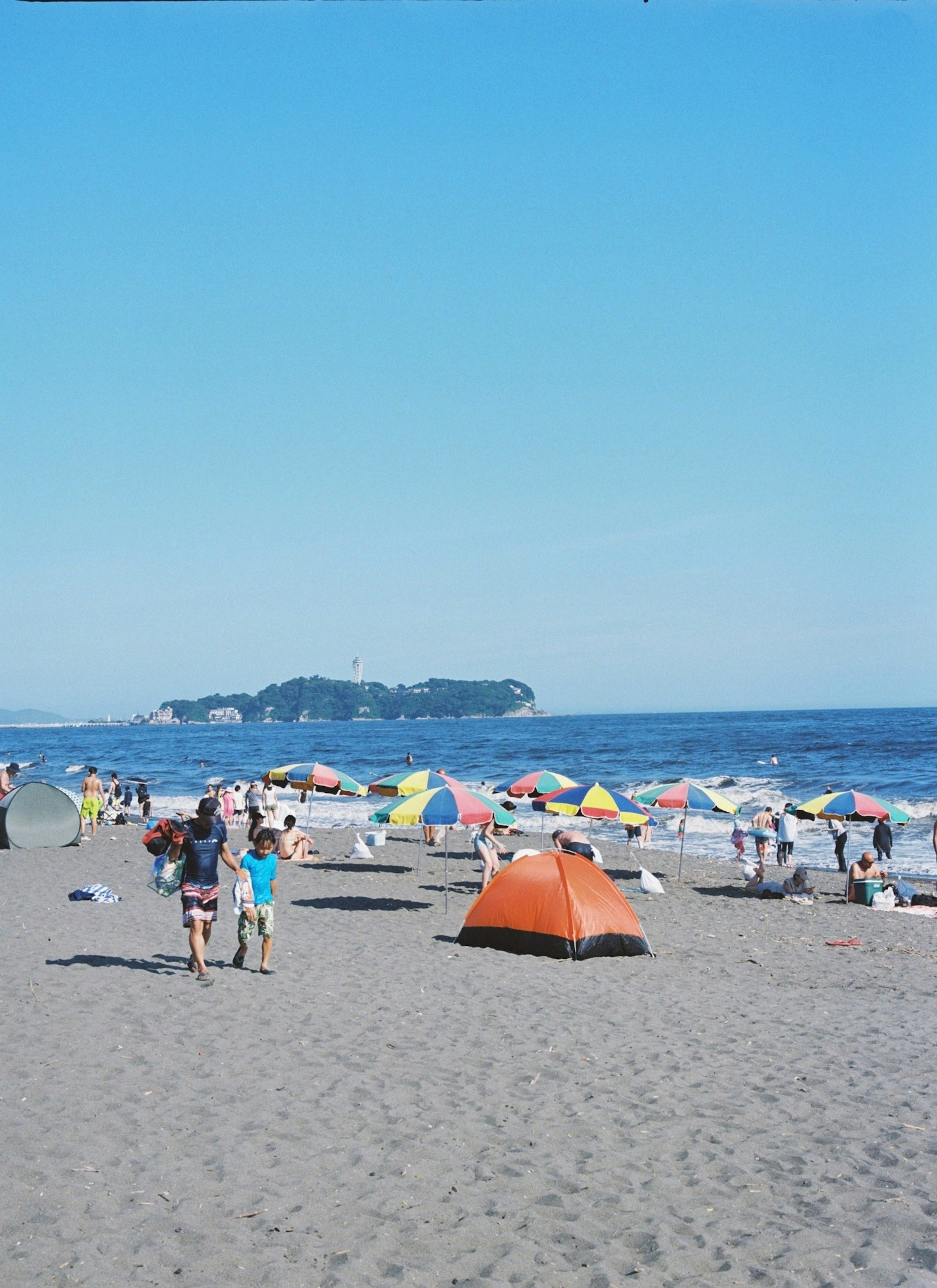 ビーチで遊ぶ人々とカラフルなパラソルが並ぶ風景