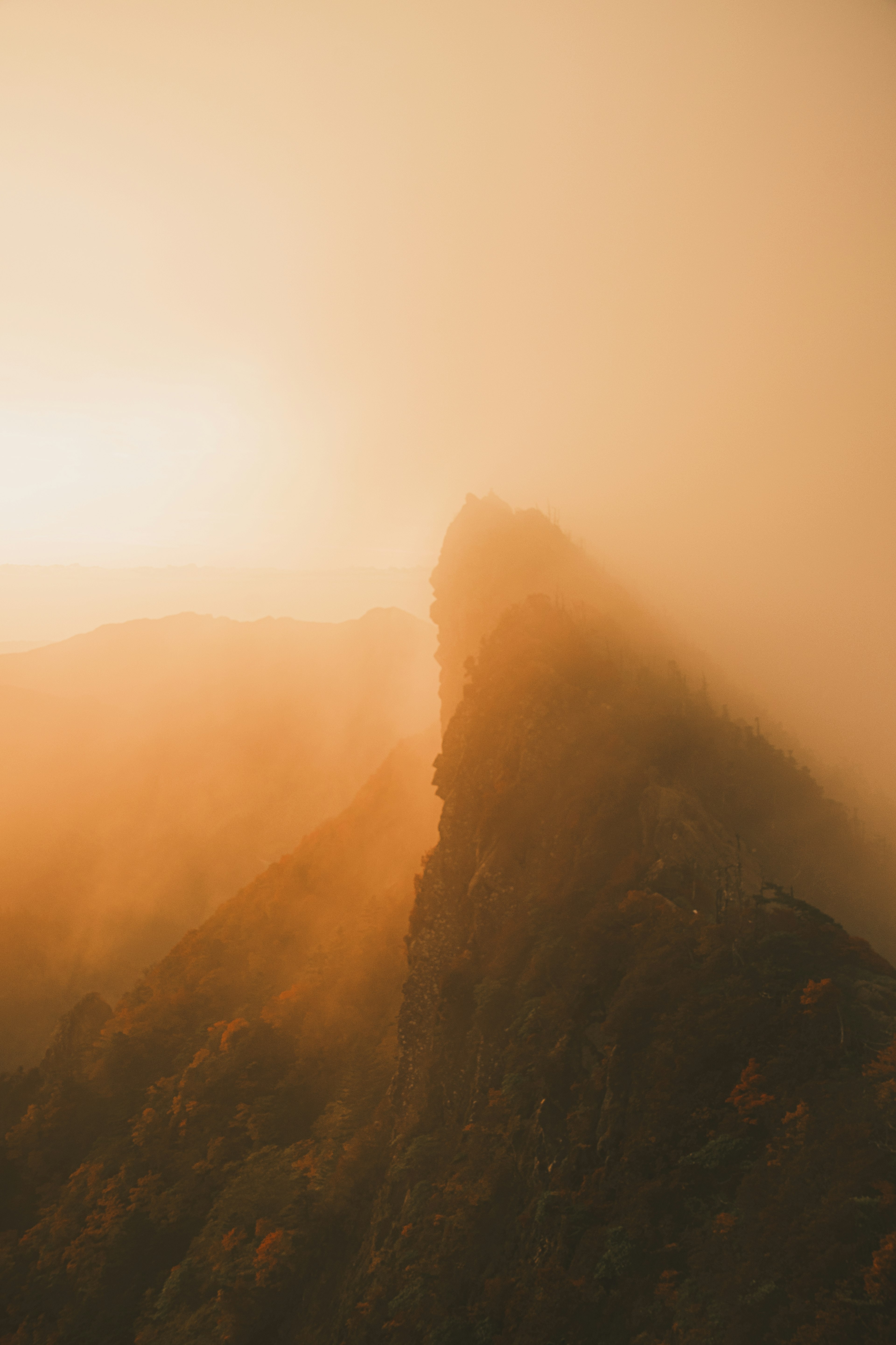 Berggipfel in Nebel gehüllt, beleuchtet von orangefarbenem Sonnenuntergang