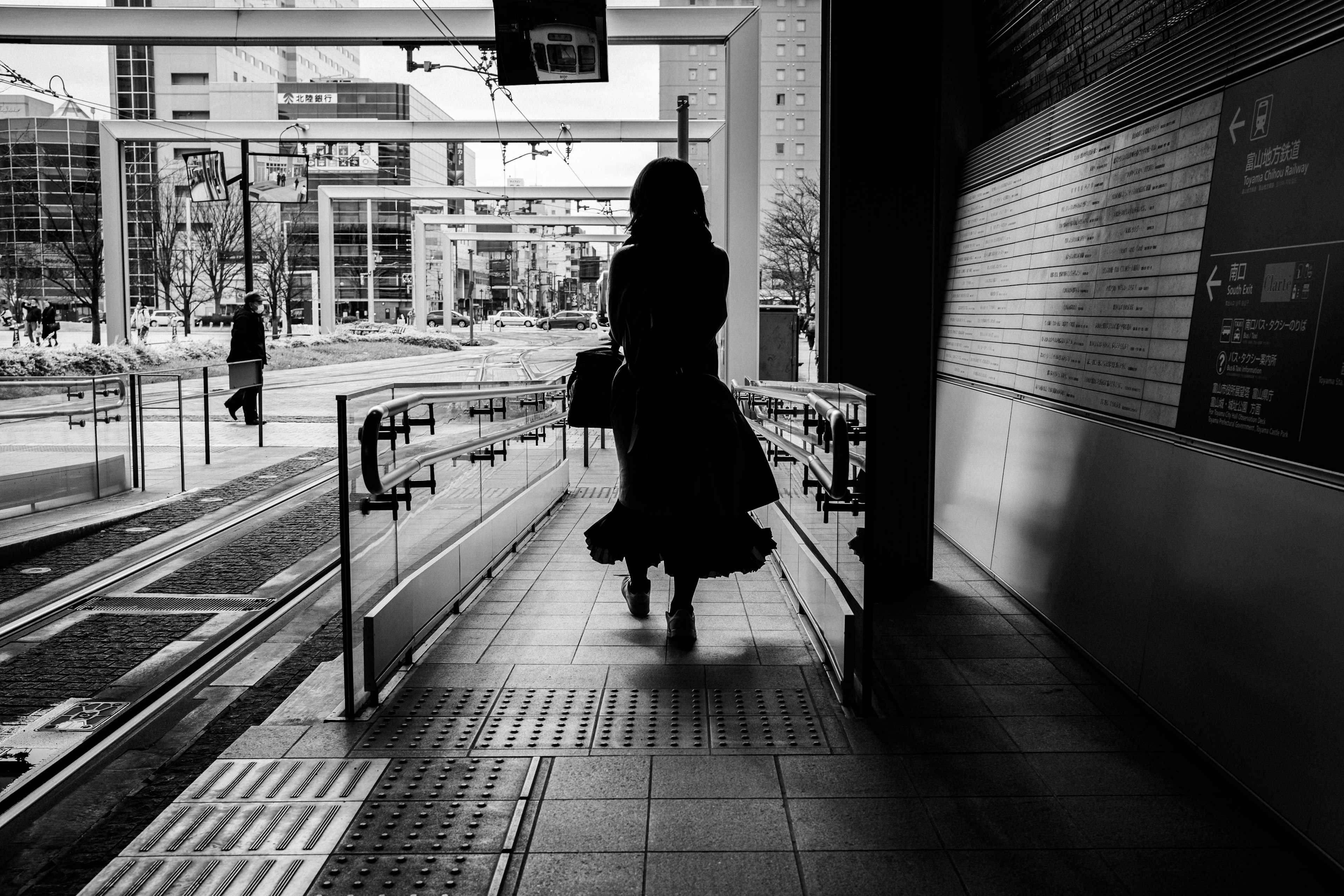 Silhouette di una donna che cammina in un contesto urbano in bianco e nero con edifici moderni sullo sfondo