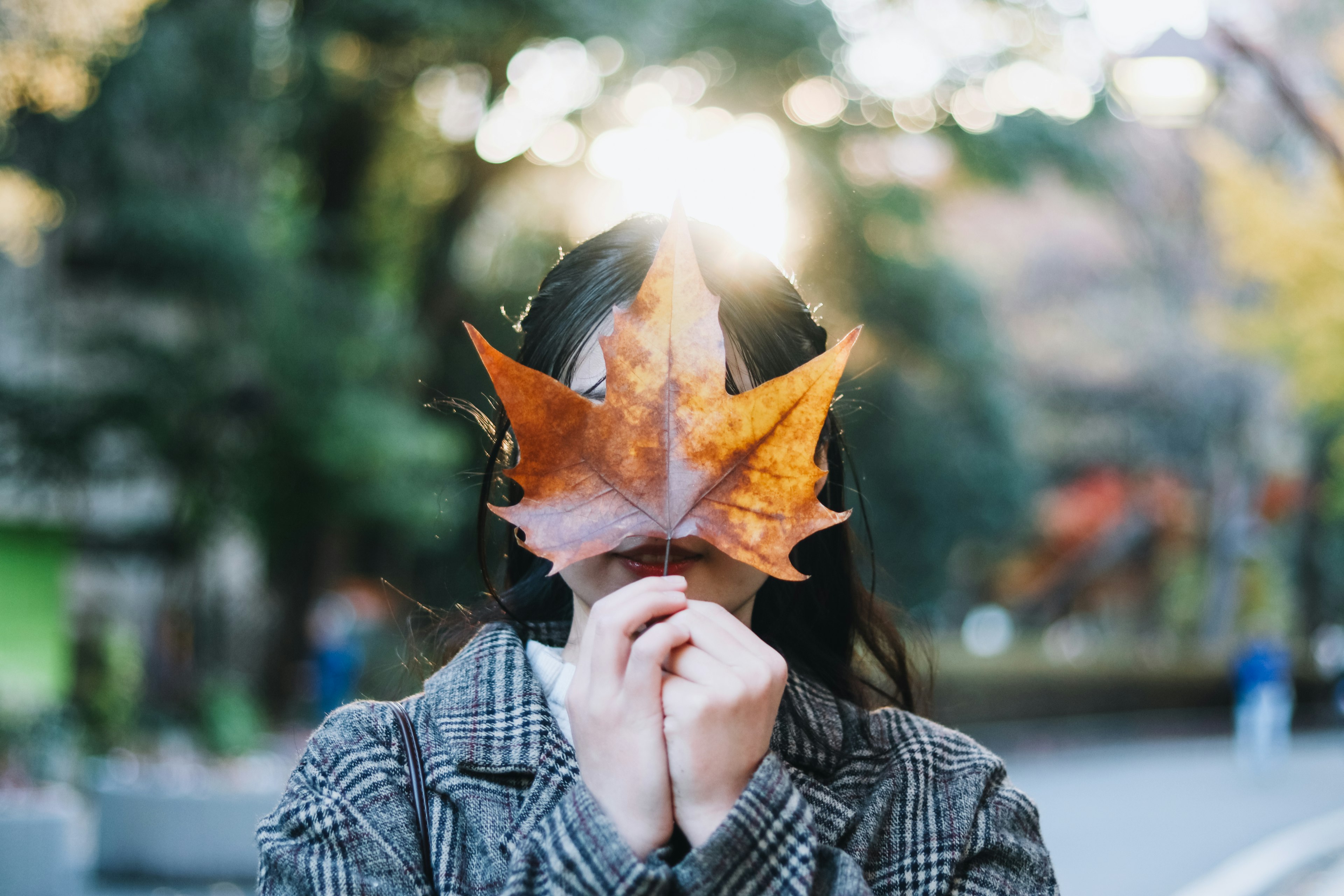 Une femme tenant une feuille d'automne devant son visage avec un arrière-plan naturel flou et une lumière douce