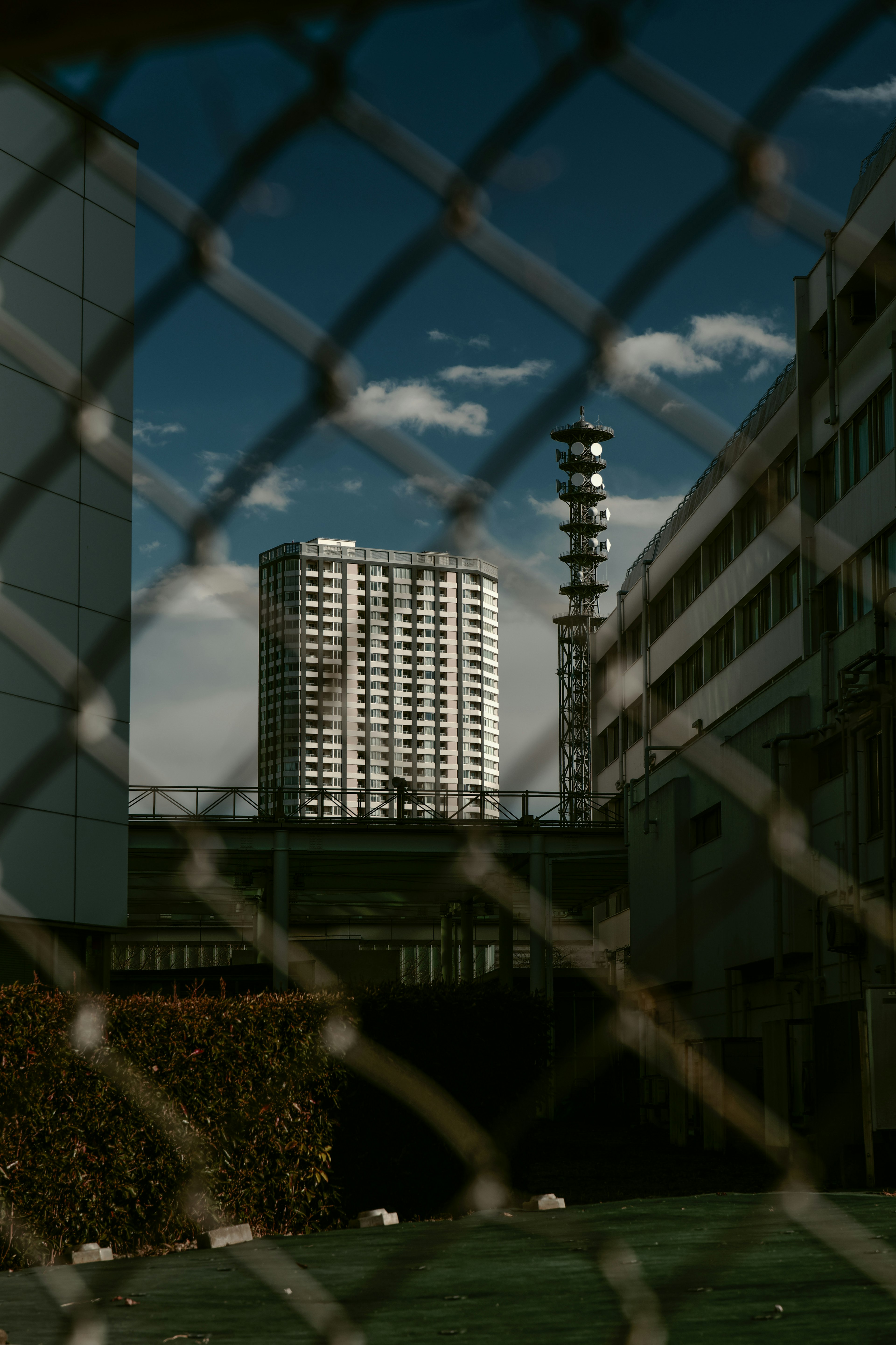 Blick auf ein Hochhaus und einen Schornstein durch einen Zaun