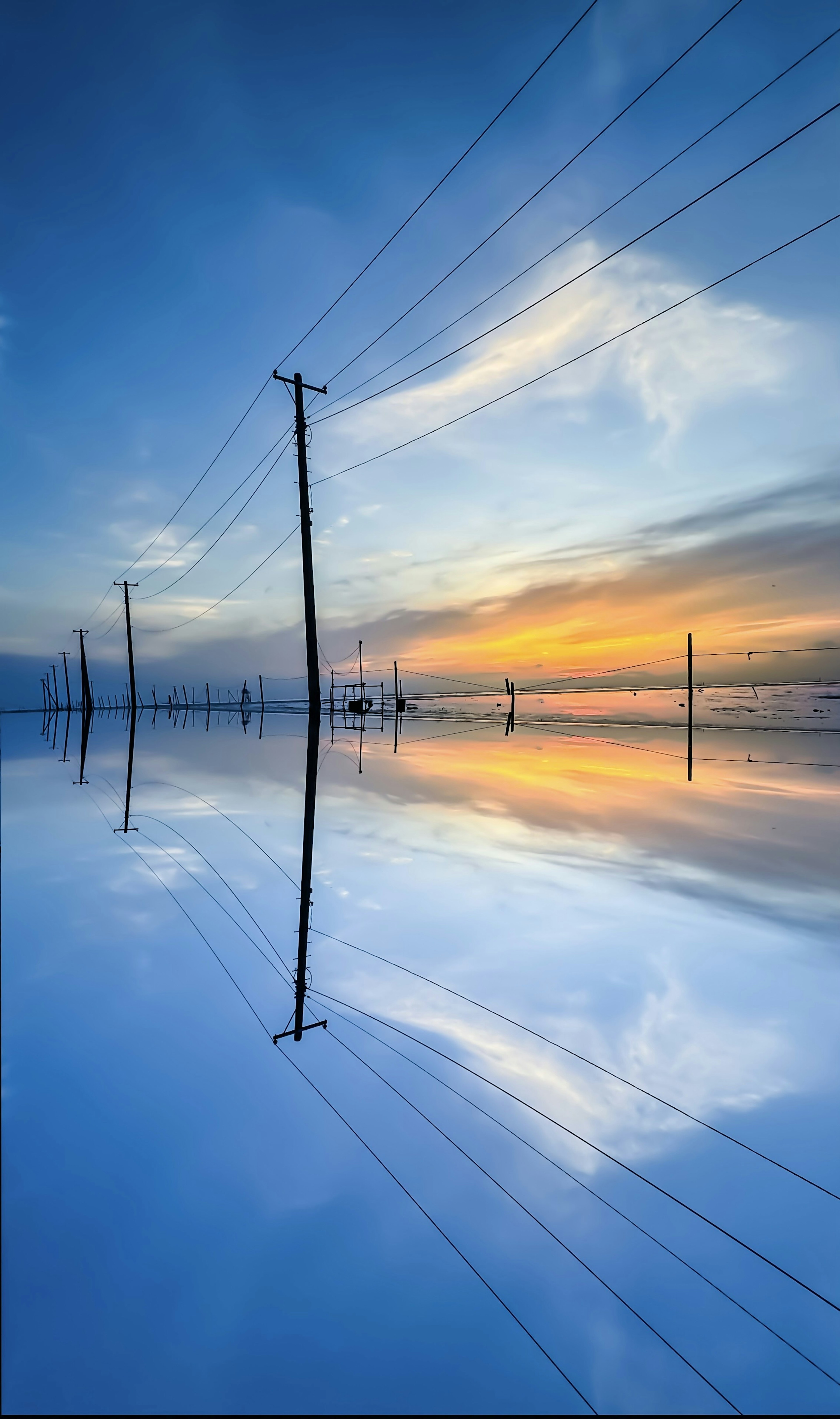 Poteaux électriques reflétés dans une eau calme au coucher du soleil avec un ciel bleu vibrant