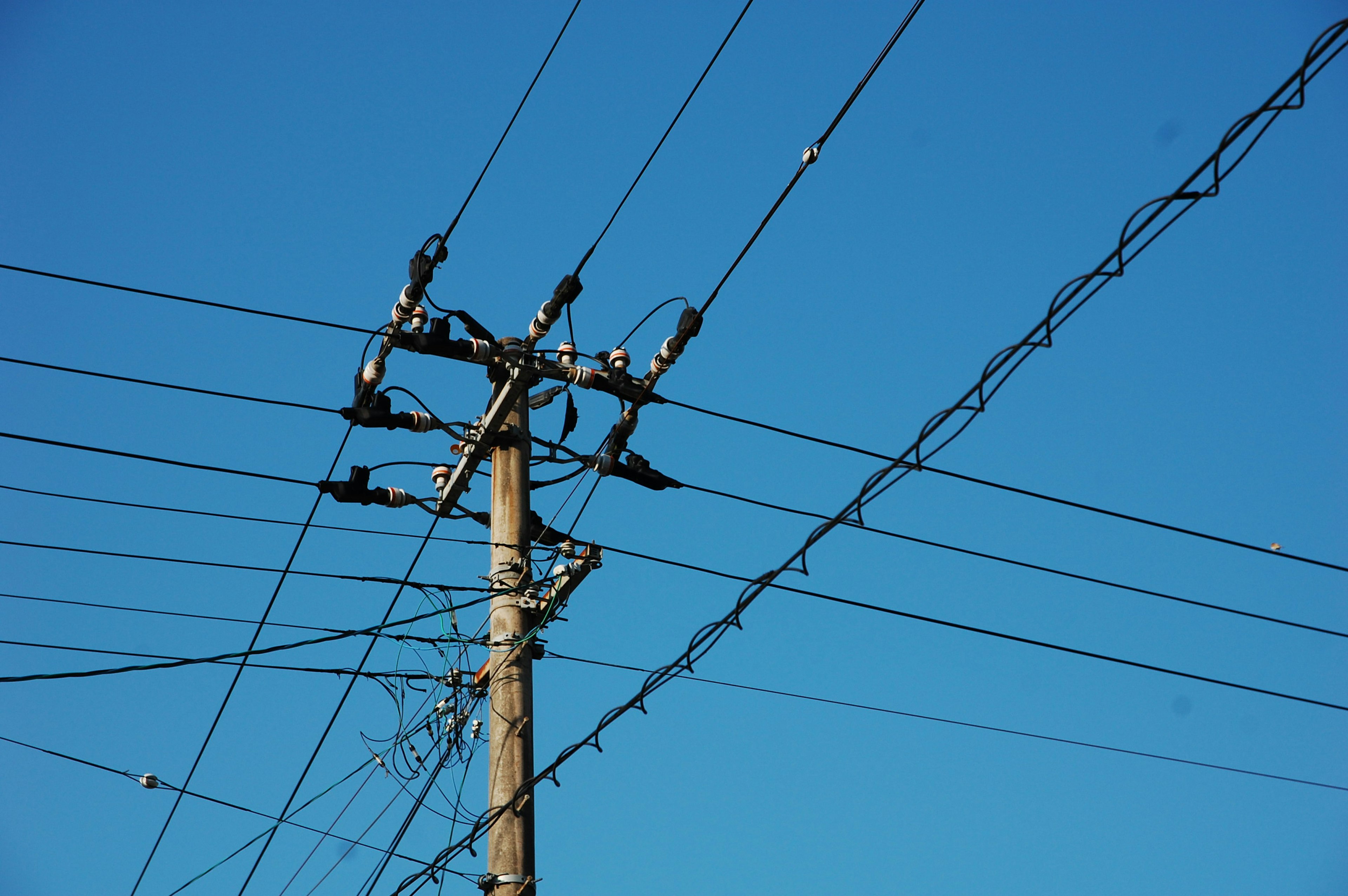 Simple scene of a utility pole and power lines against a blue sky