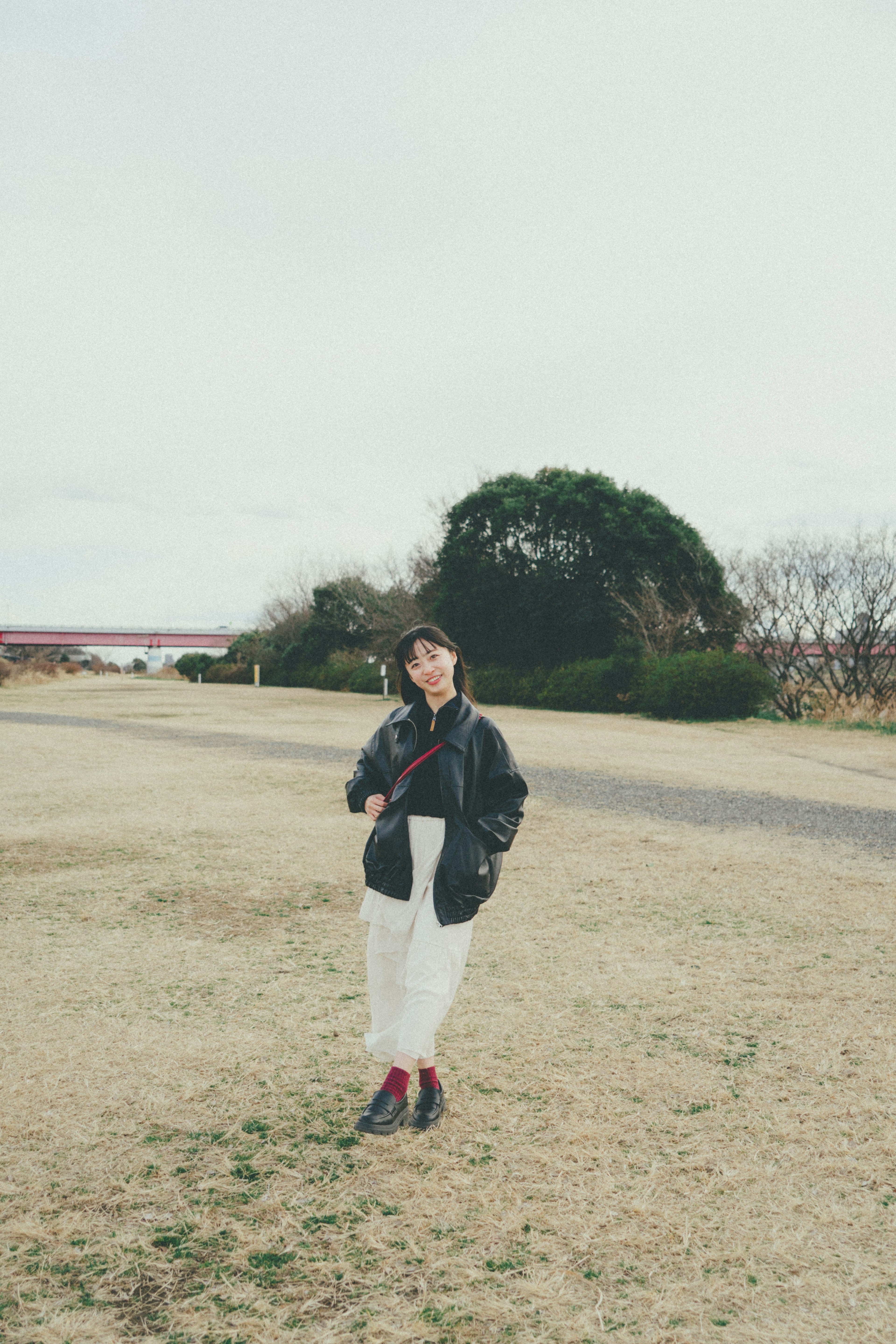 女性が公園で立っている風景 寒い季節の服装と草地