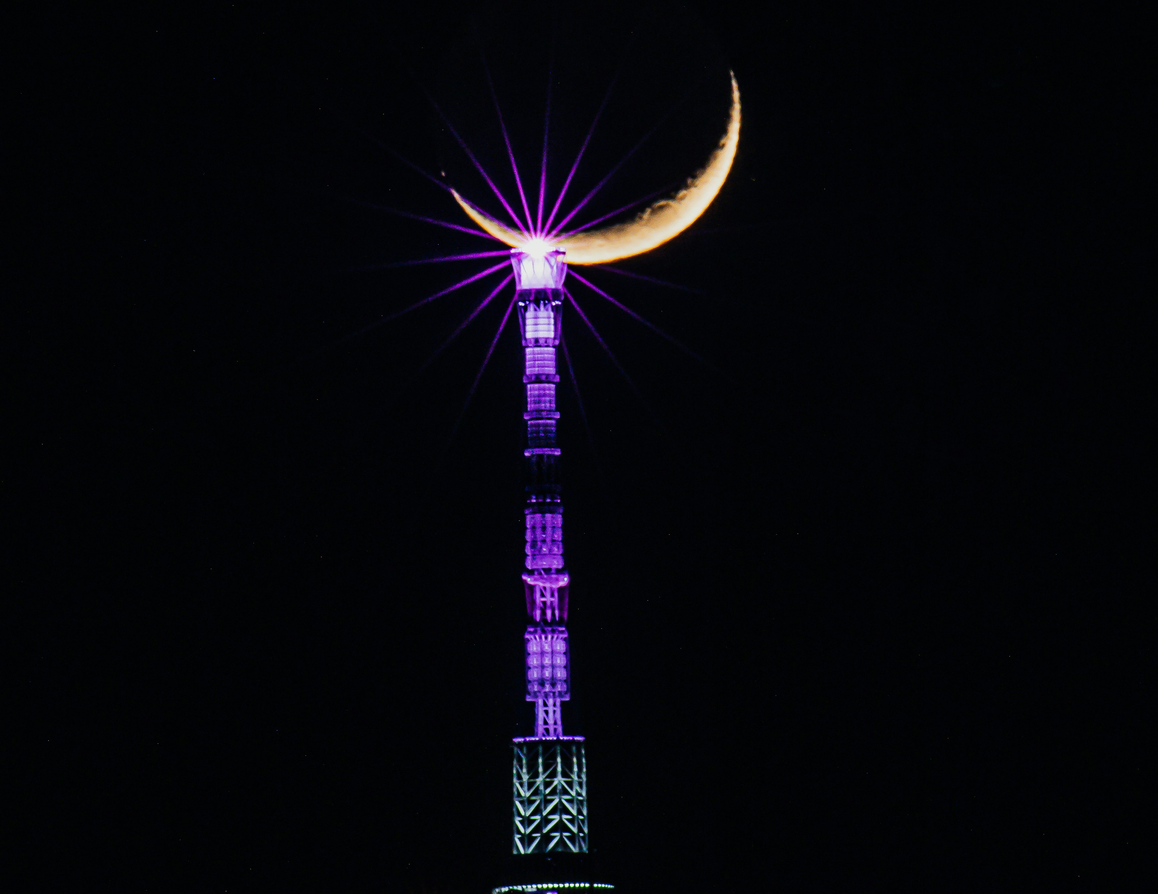 Una luna creciente brillando en la cima de una torre iluminada de púrpura contra un cielo oscuro