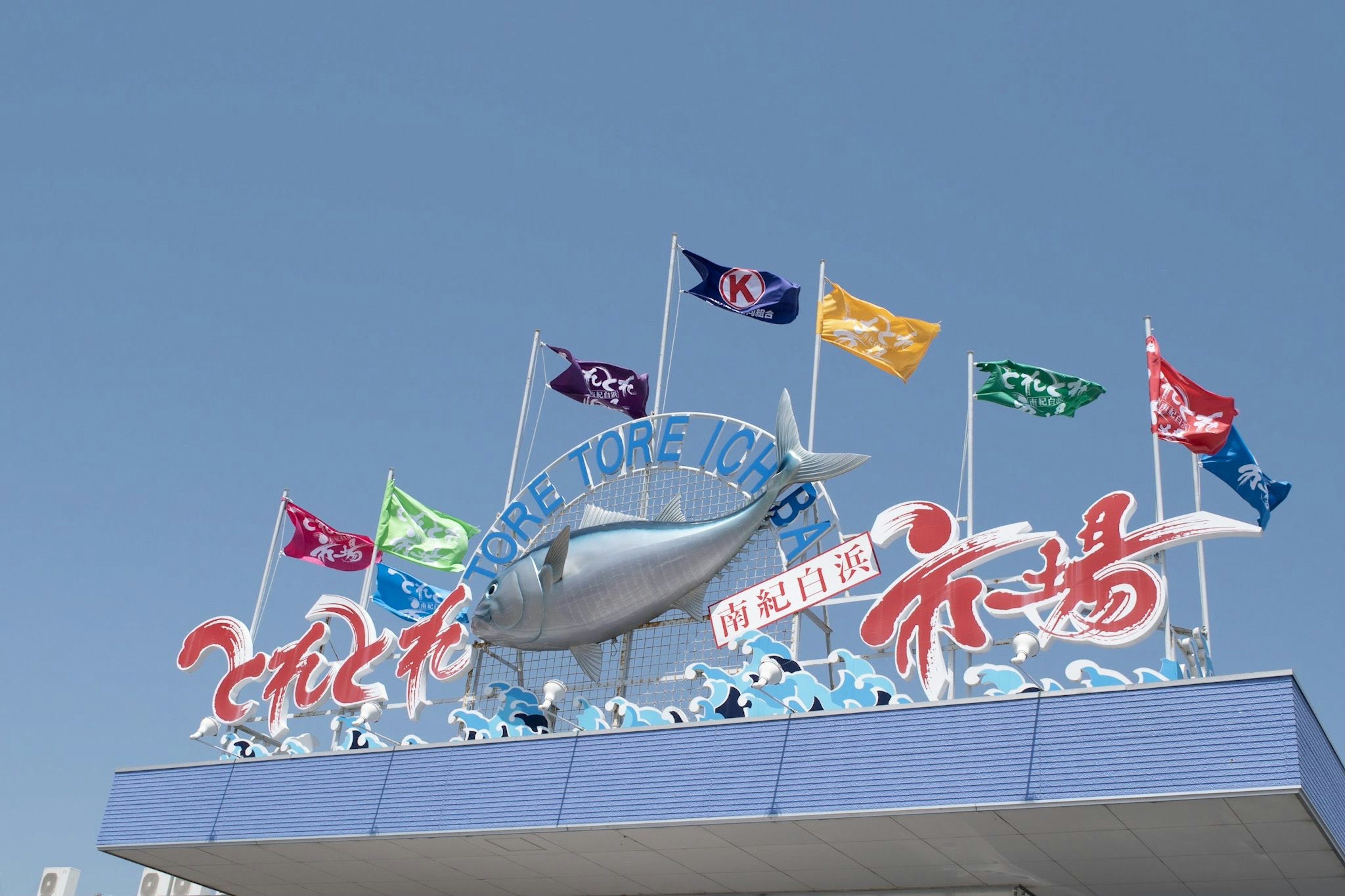 Sign with colorful flags and a large fish sculpture under a clear blue sky