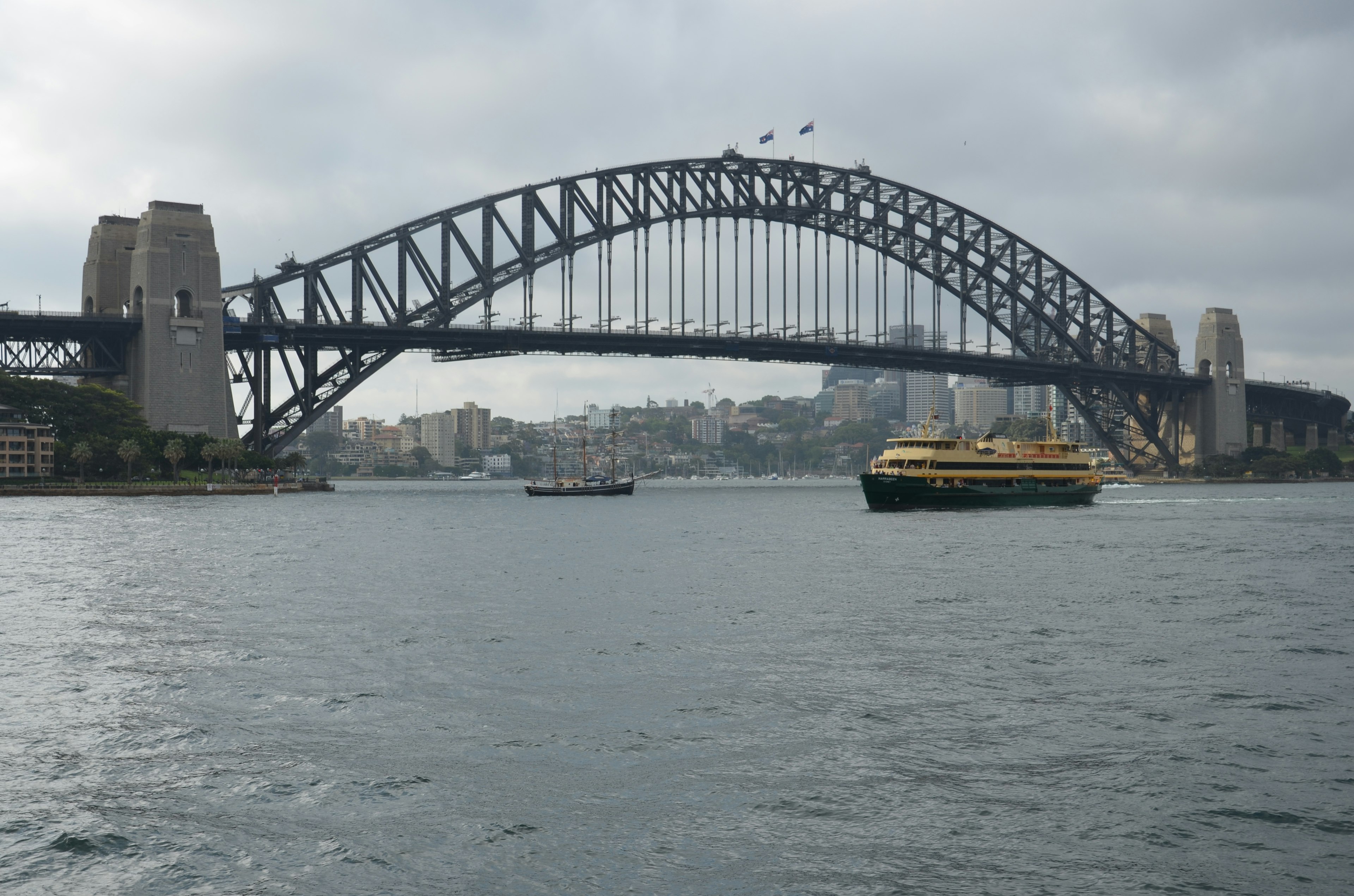 Jembatan Pelabuhan Sydney dengan feri di atas air mendung