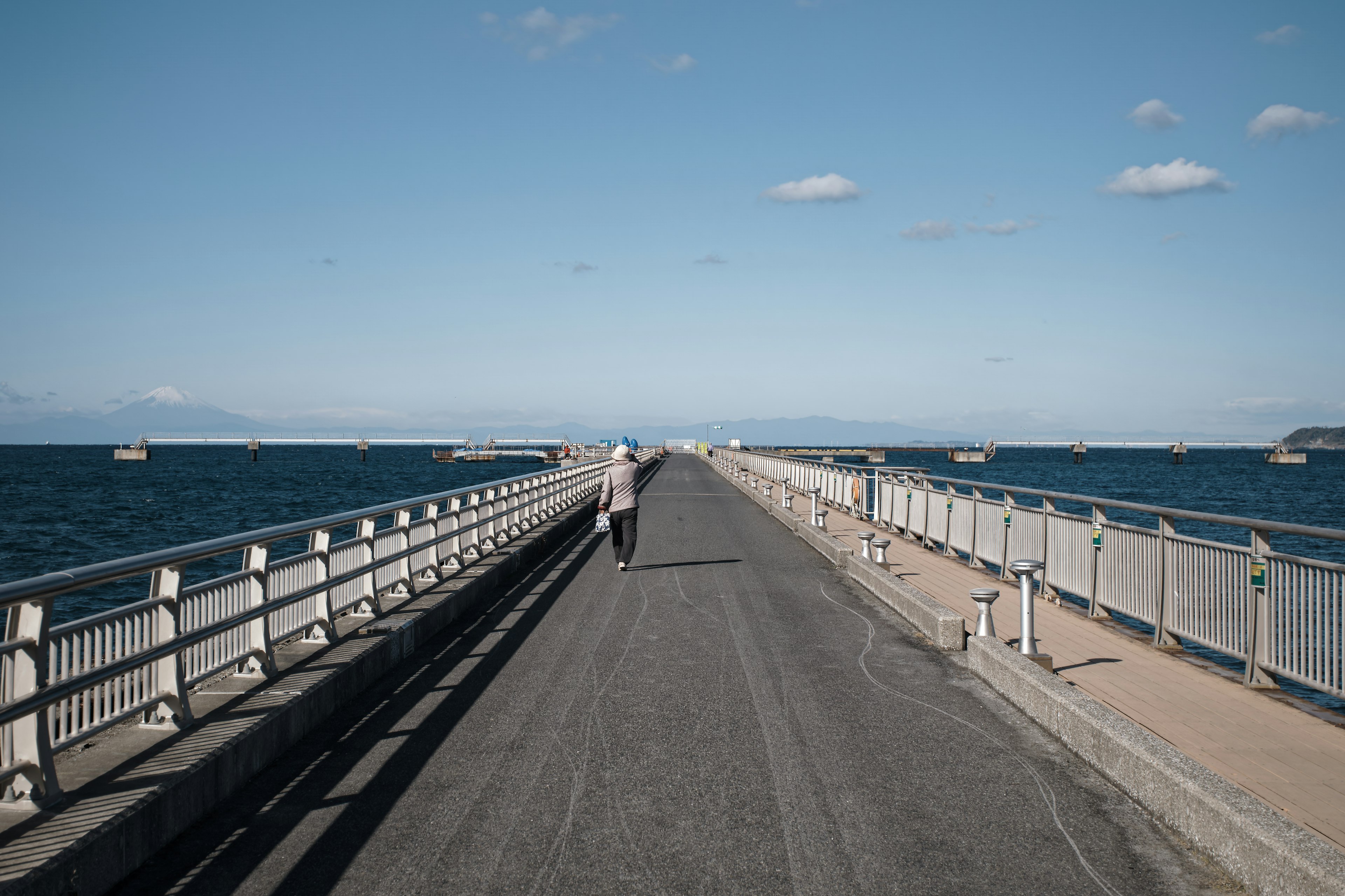 A long pier with a person walking towards the sea