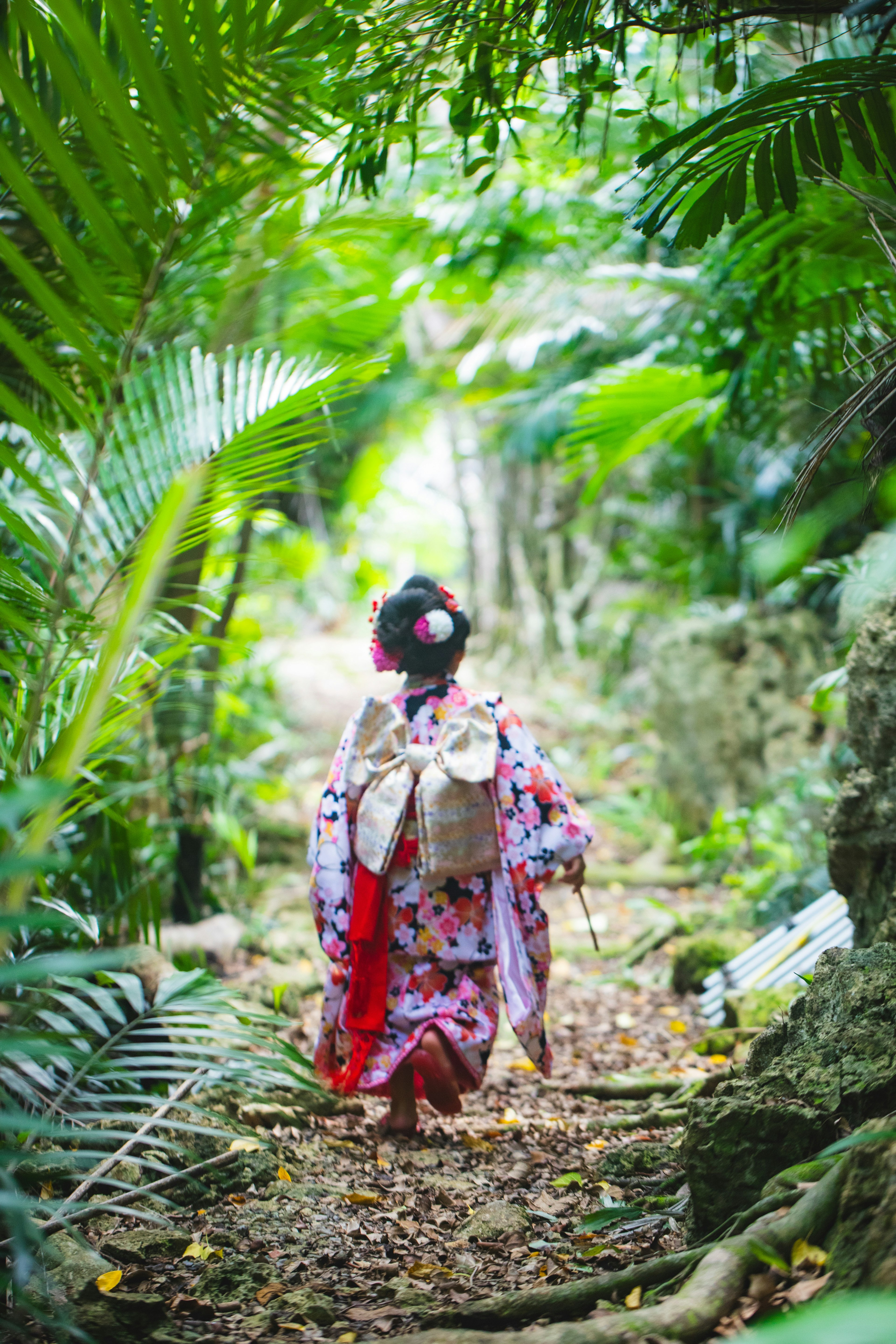 Wanita berpakaian kimono tradisional berjalan di sepanjang jalan setapak yang rimbun di hutan