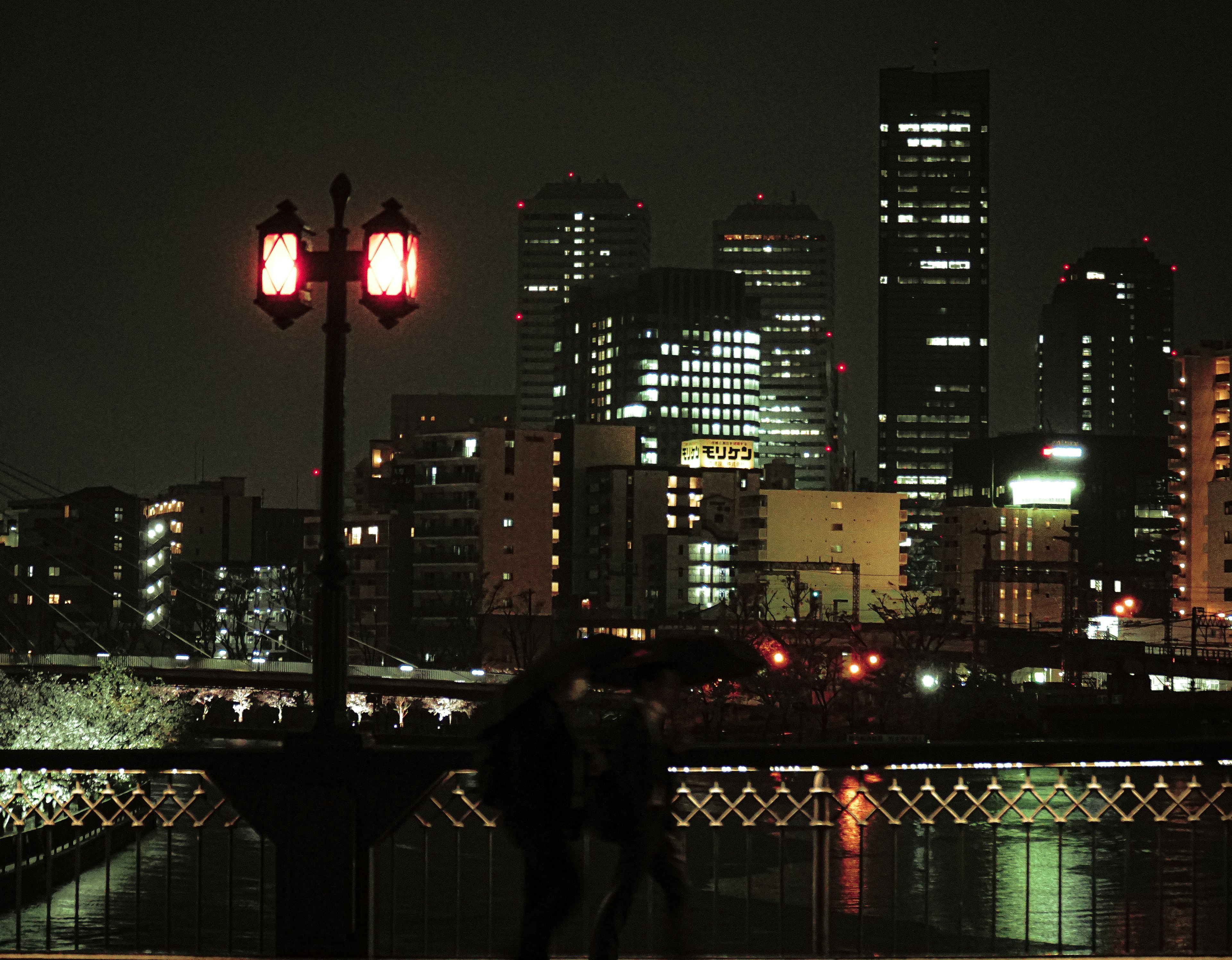 Paysage urbain nocturne avec des bâtiments éclairés et des gens au bord de la rivière