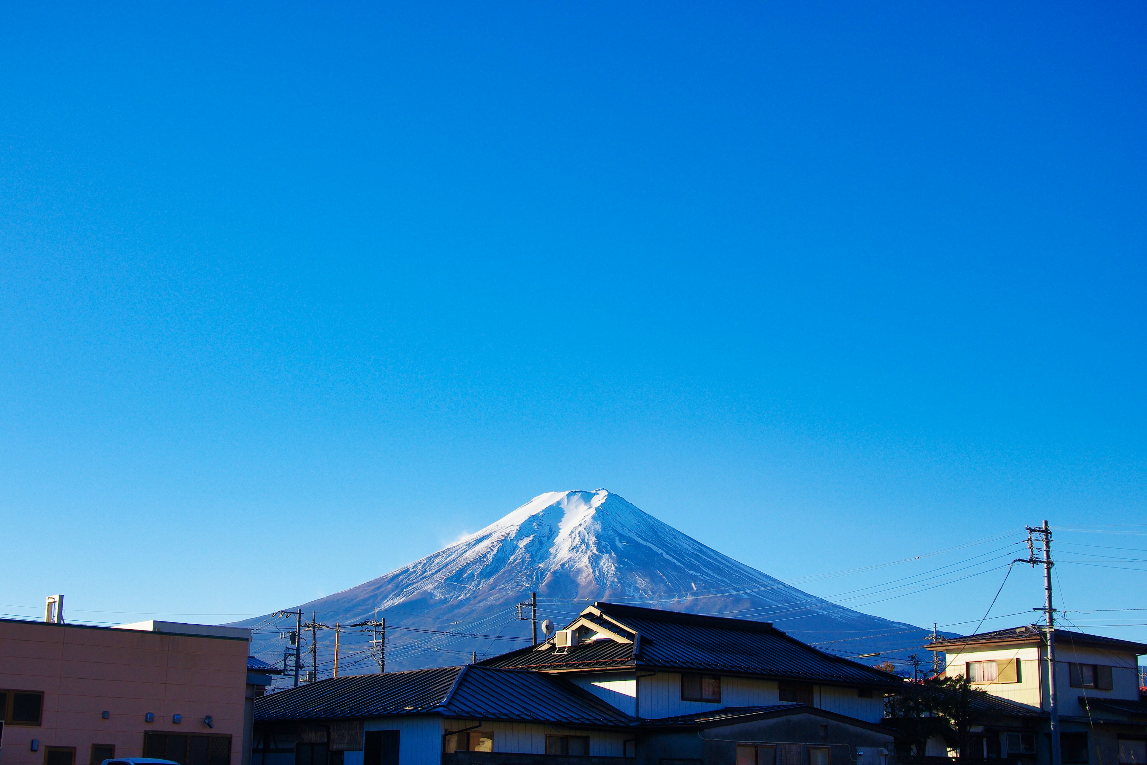 Monte Fuji innevato sotto un cielo blu chiaro con edifici circostanti