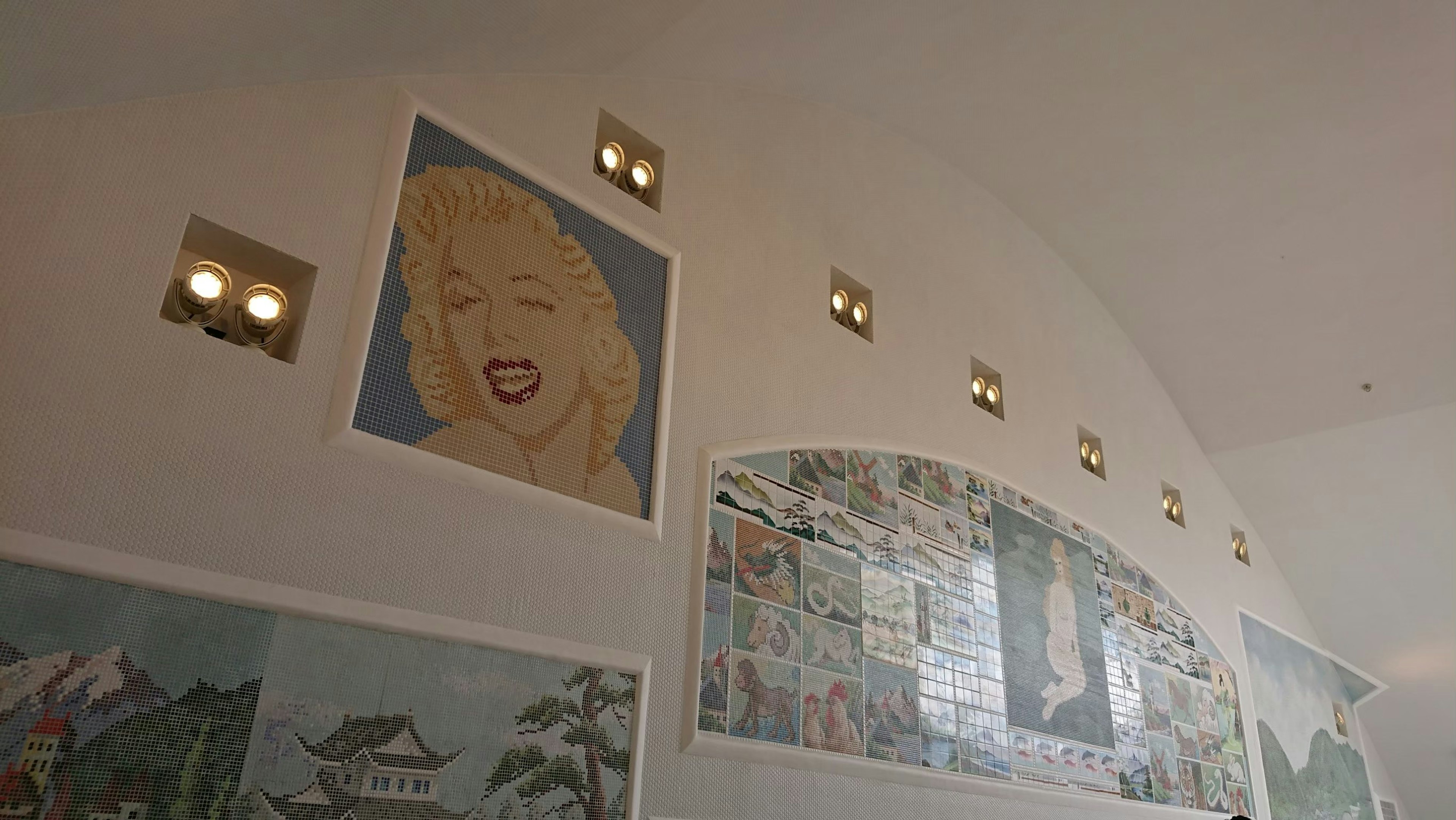 A large portrait of Marilyn Monroe on a white wall with multiple art pieces displayed