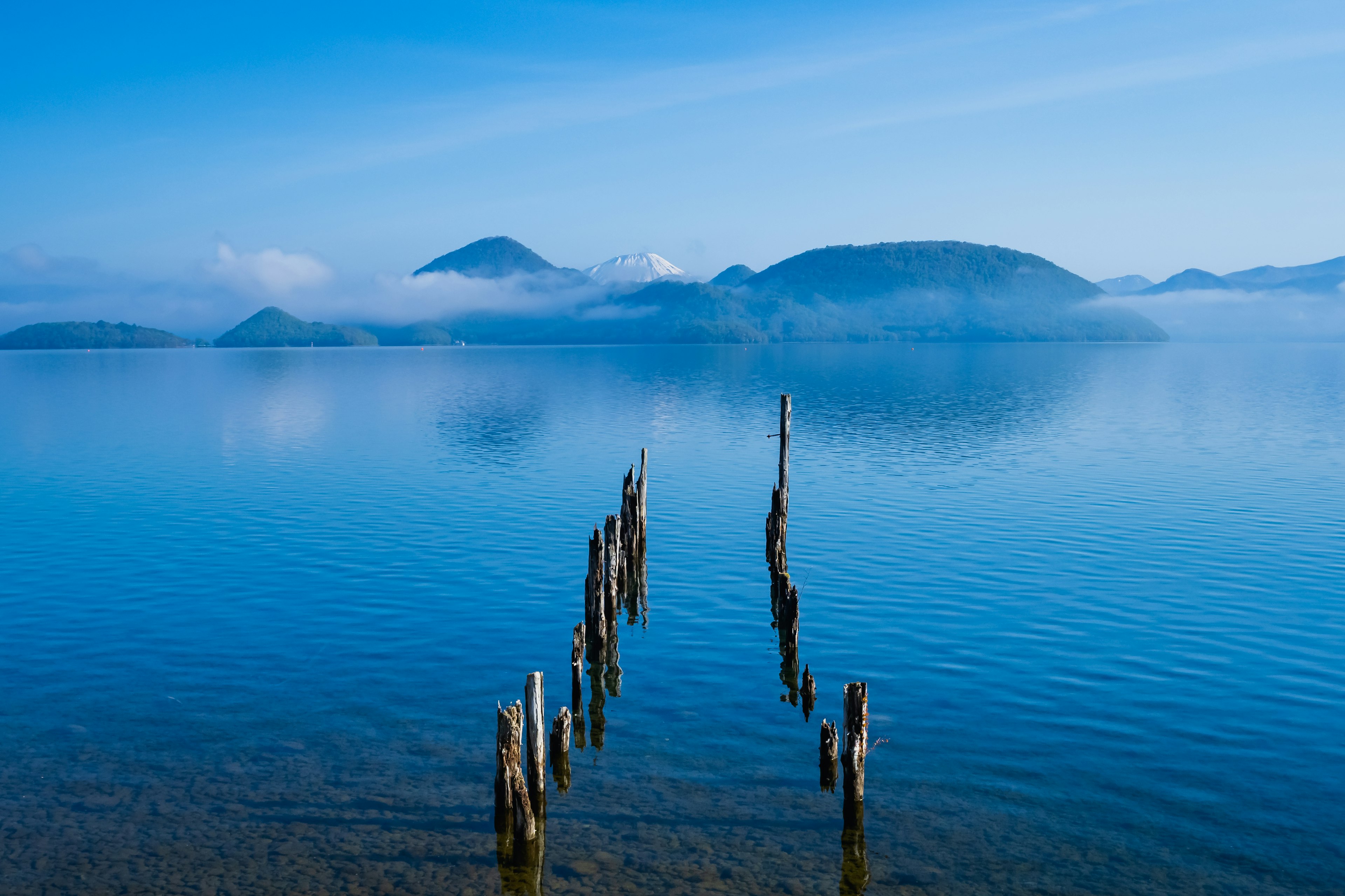 Pemandangan tenang danau dengan gunung berkabut tiang kayu tua di air